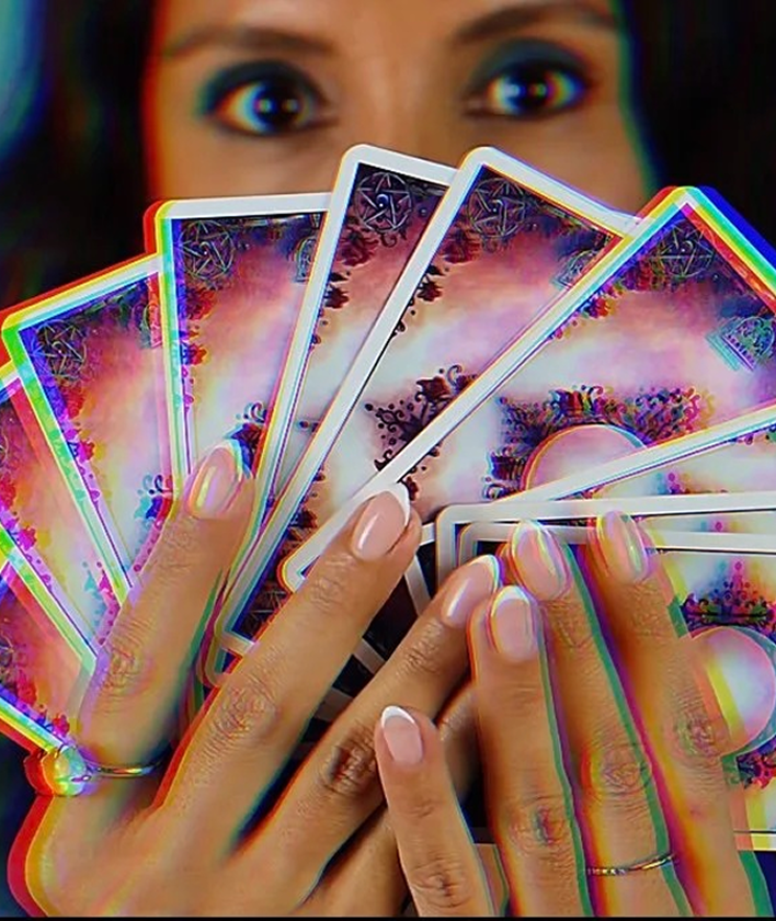 A person holding colorful tarot cards in front of their face, with only their eyes visible in the background.