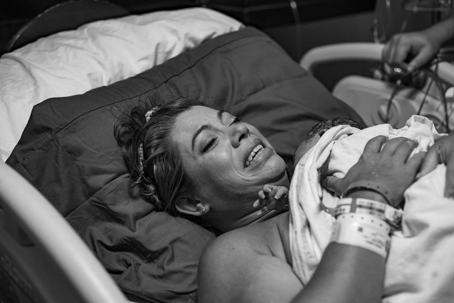 mom crying "i am so happy" with her newborn daughter on her chest while dad looks down at her from beside the bed.