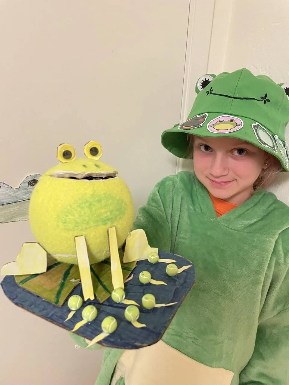   Uli  (9 years old)   Tennis Frogster , 2026  Tennis balls, cardboard, beads   Description:  Did you know that most tennis balls dream of becoming a frog? But only a few get a chance to become one...just like this one!   Artist background:  Uli is a