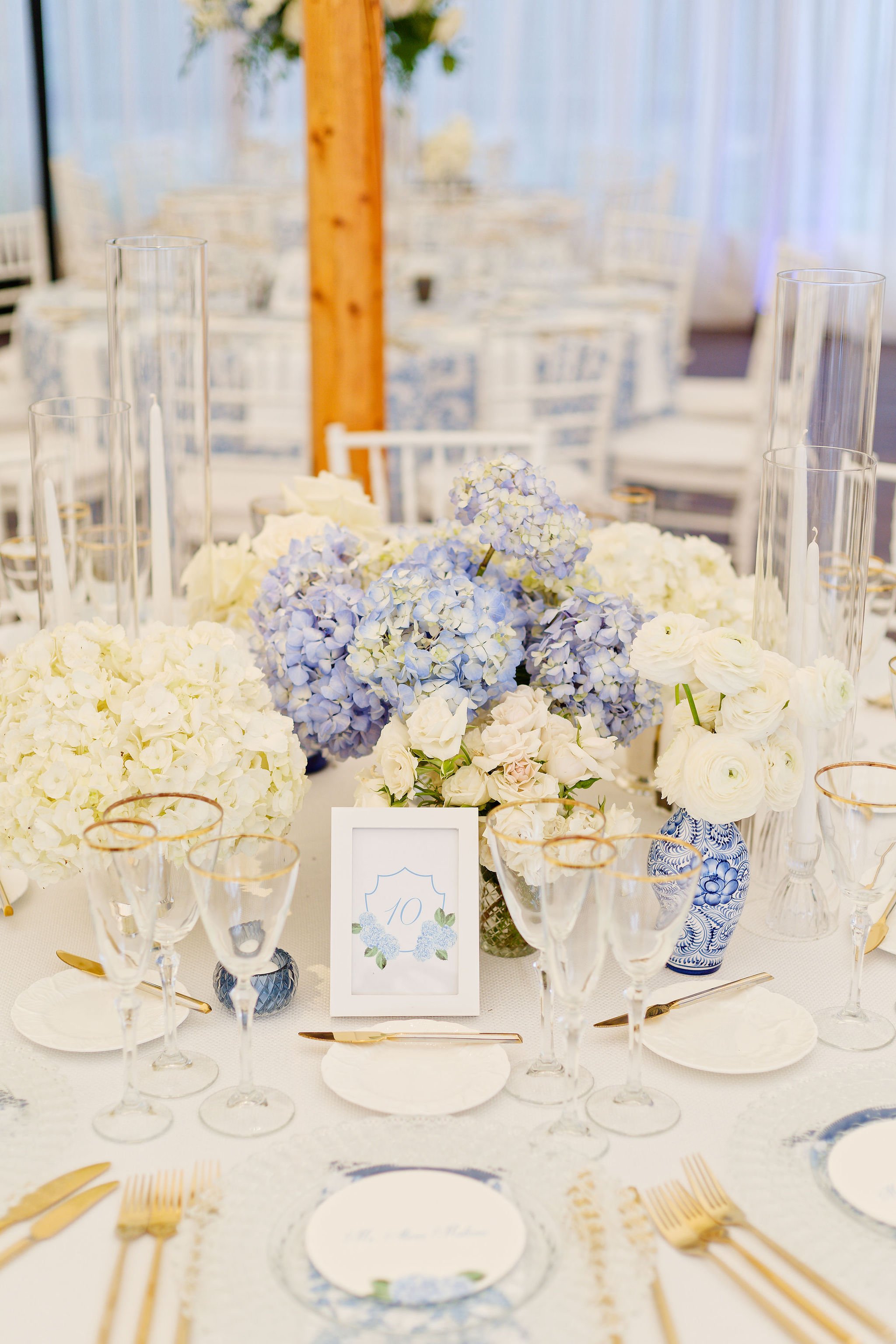 Elegant table setting with white and blue floral centerpiece, gold flatware, glassware, and a table number 10