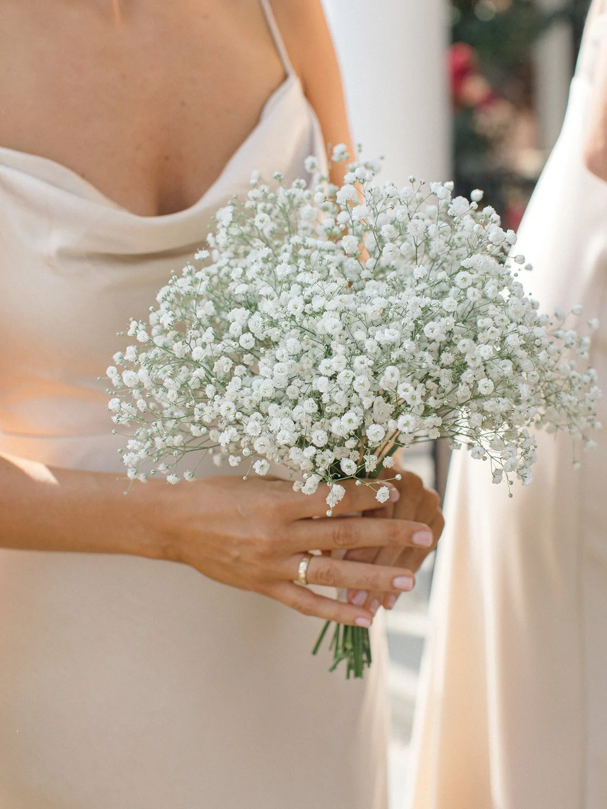 Someone holding a bouquet of white baby's breath flowers, wearing a white dress with a cowl neckline.
