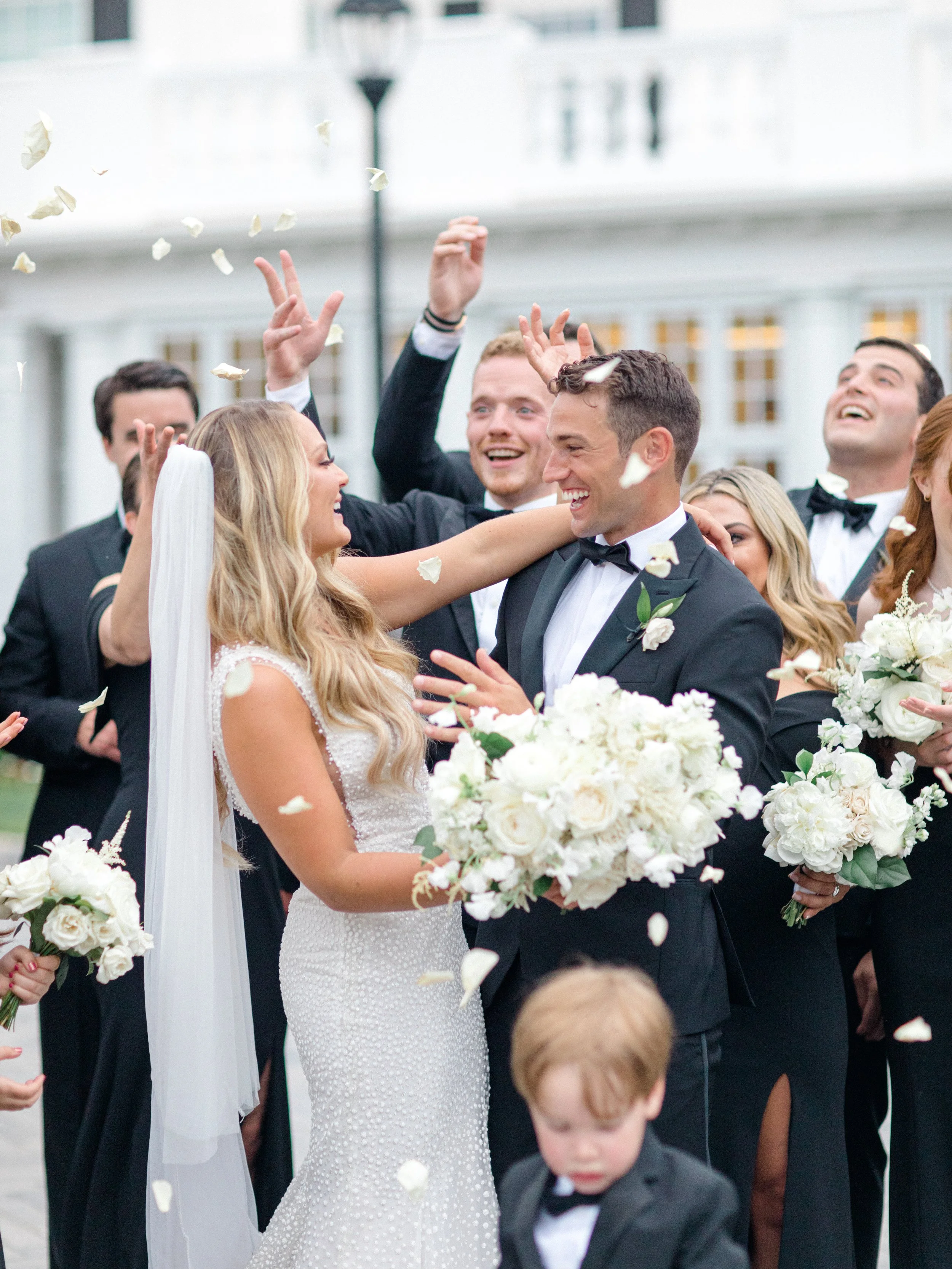 Bride and groom celebrating with friends and family outside, wedding flowers, confetti, and happy expressions.