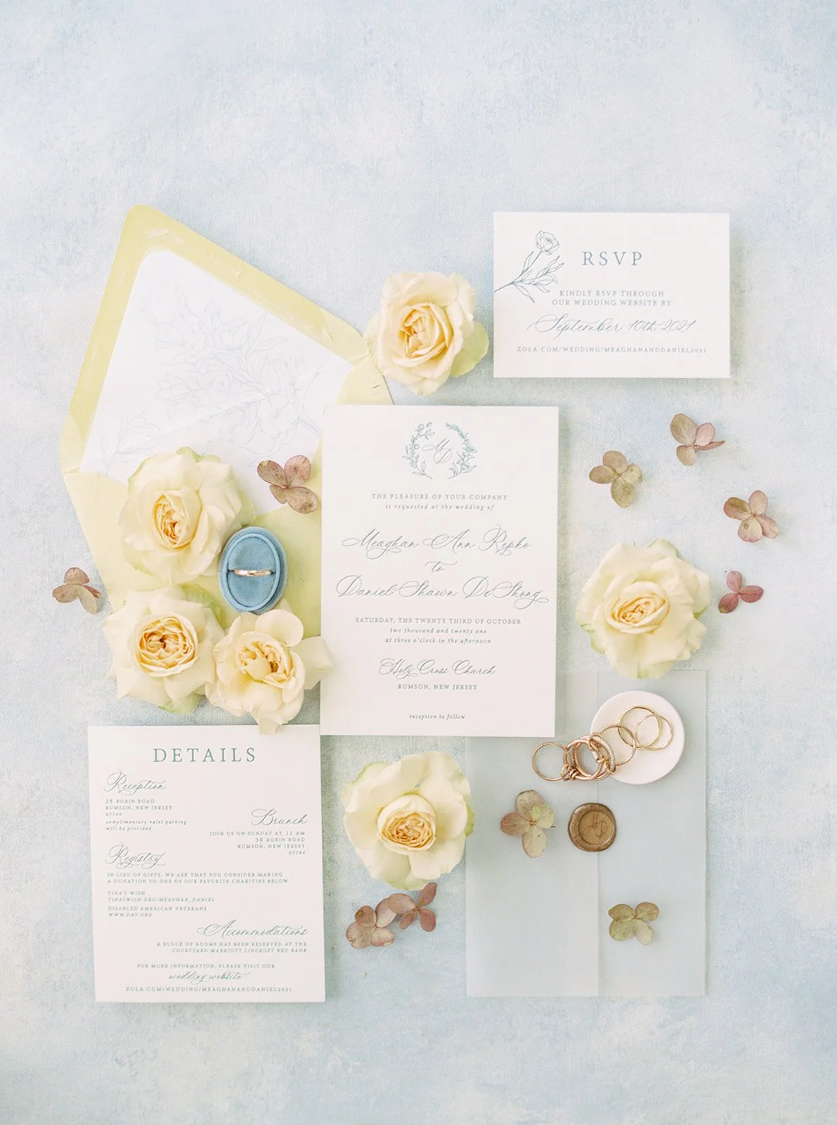 Wedding invitations, RSVP card, rings in a blue velvet box, dried flowers, and a wax seal on a light background.