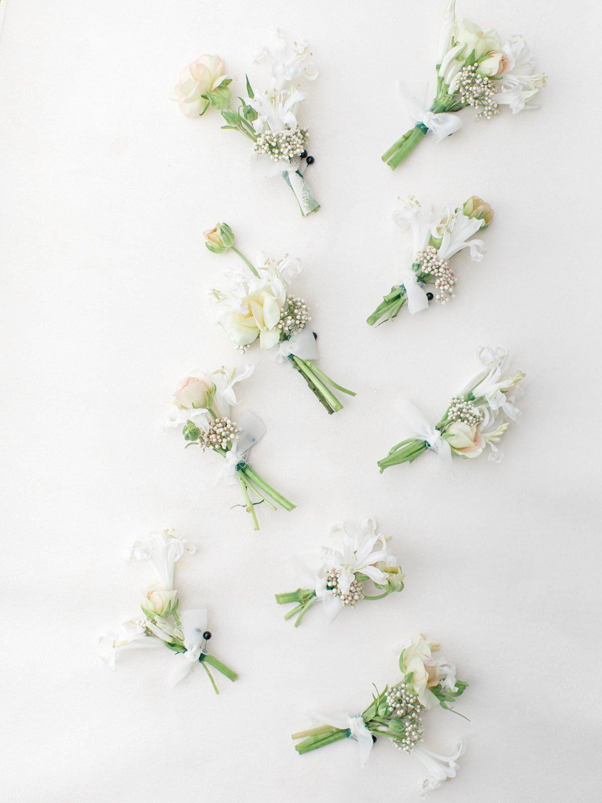 Multiple small boutonnieres with white and pale pink flowers arranged on a white background.