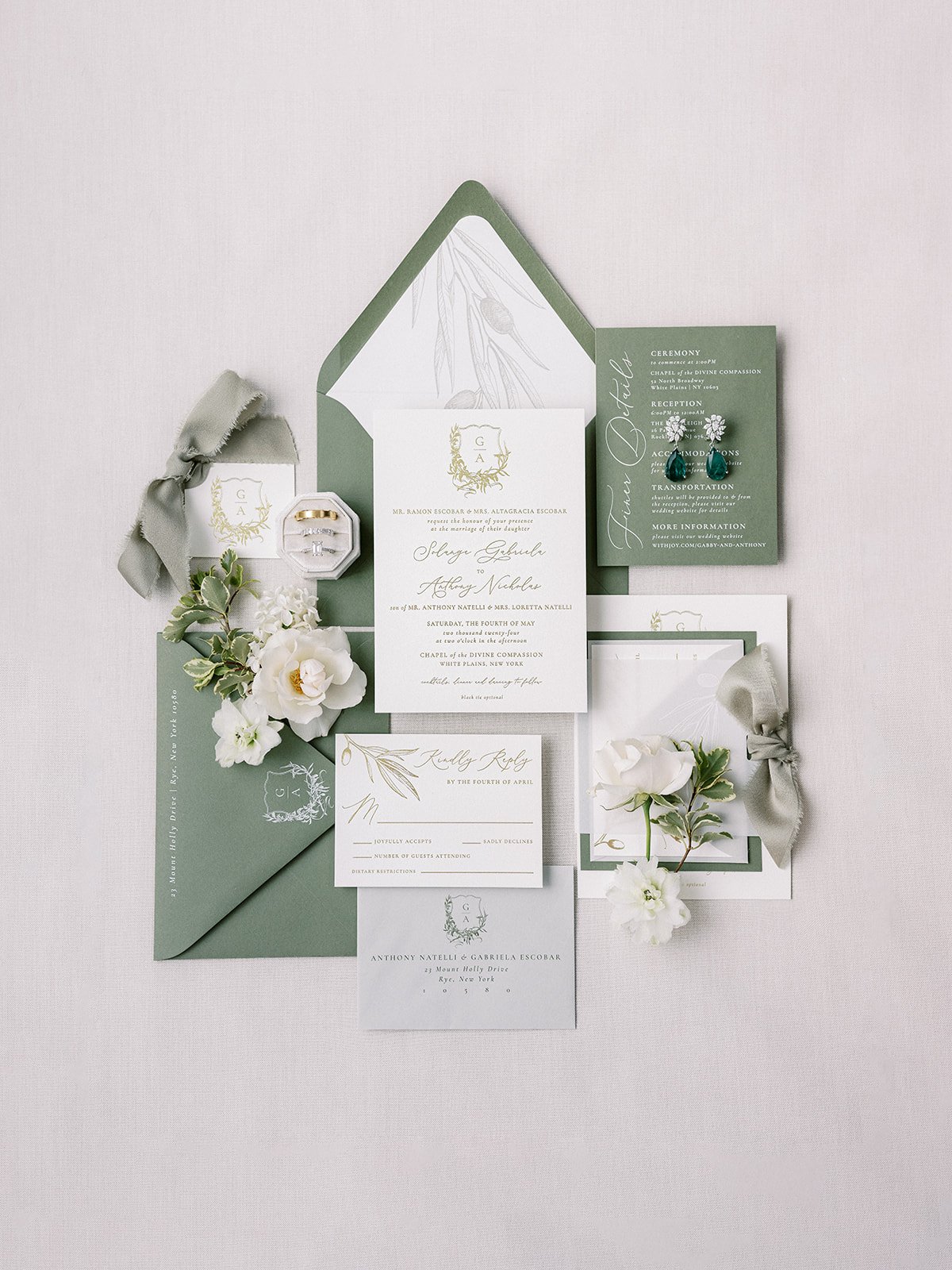 Wedding invitation suite with green, white, and gold accents, flowers, and jewelry displayed on a white background.