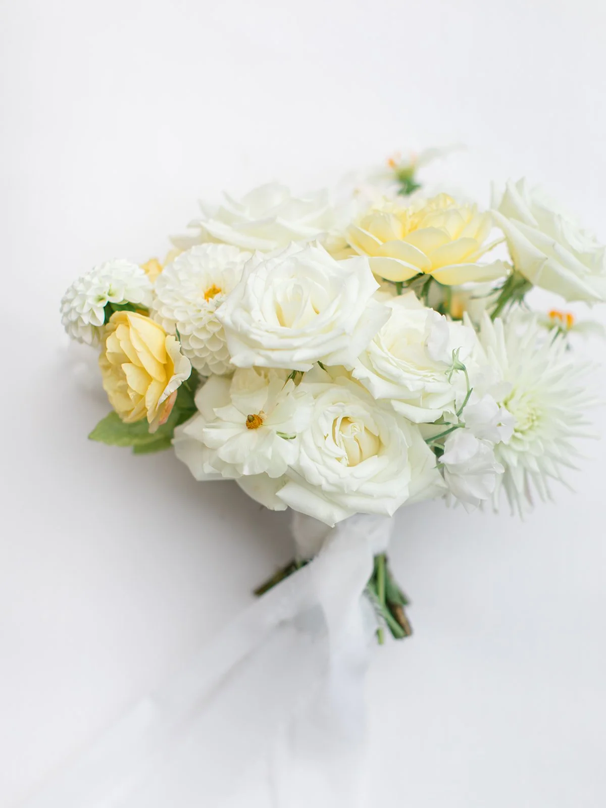 A bouquet of white and pale yellow flowers with a white ribbon, set against a white background.