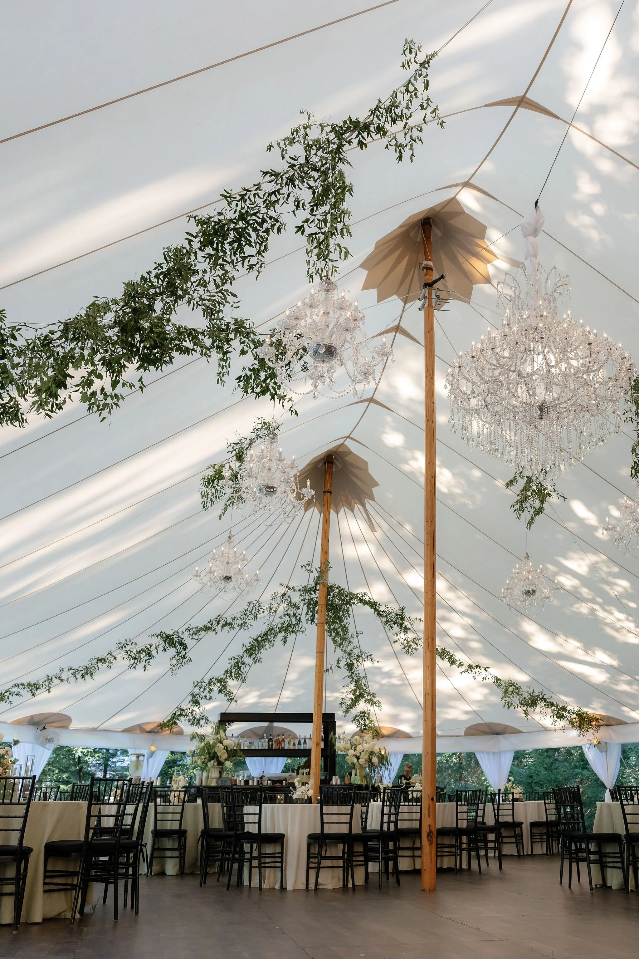 A decorated event tent with chandeliers, greenery, and tables set for a celebration or wedding.