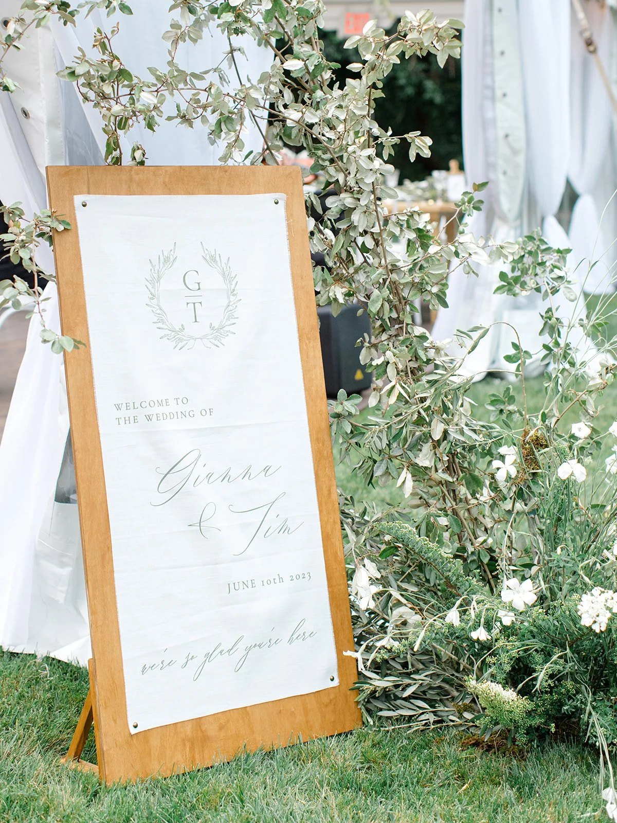 Wedding welcome sign featuring the initials G T and the names Gianna and Tim, with the date June 10th, 2023, surrounded by greenery and flowers.