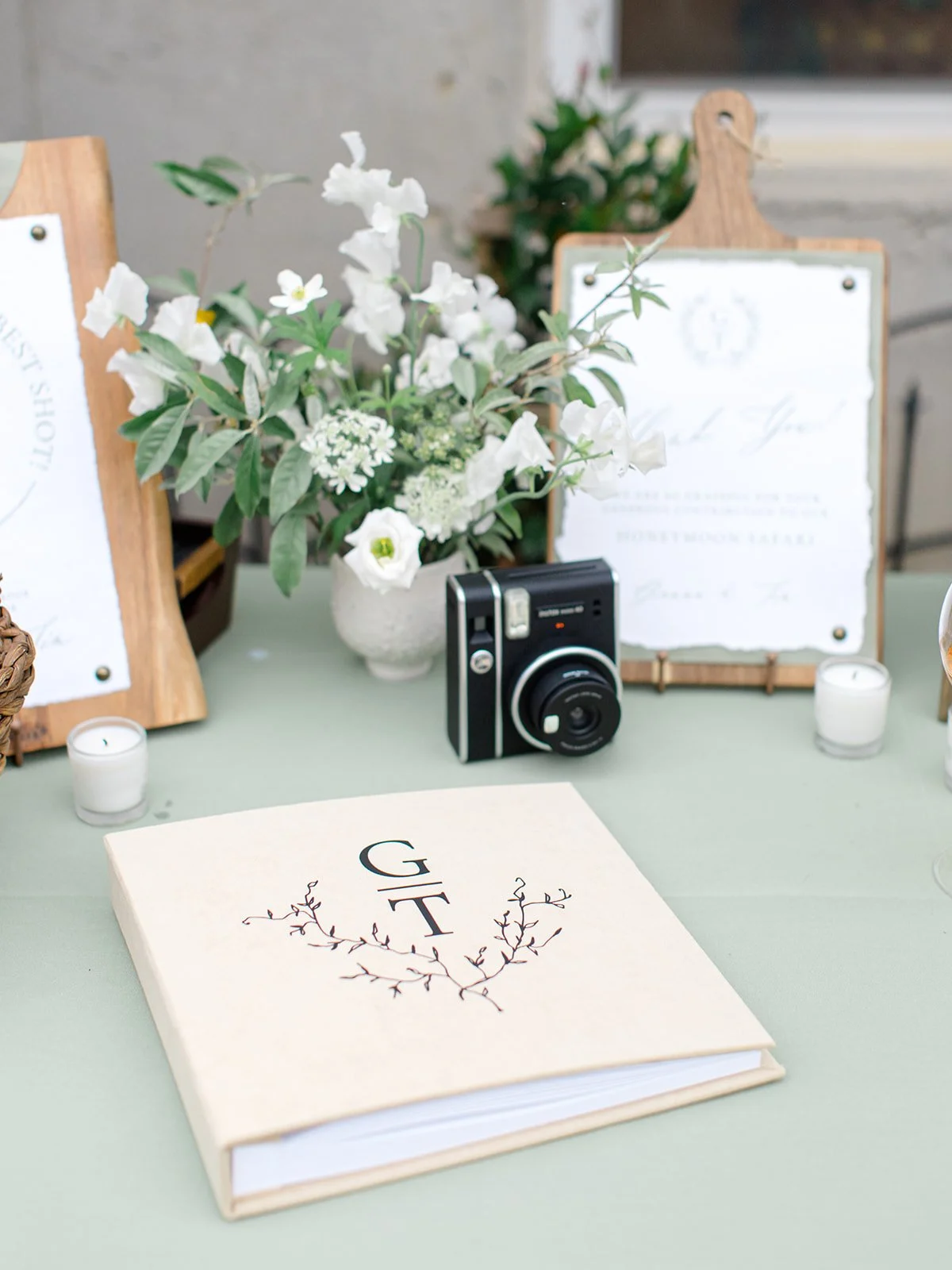 Wedding guest book, vintage camera, floral arrangement, candles, and framed wedding invitation on table.