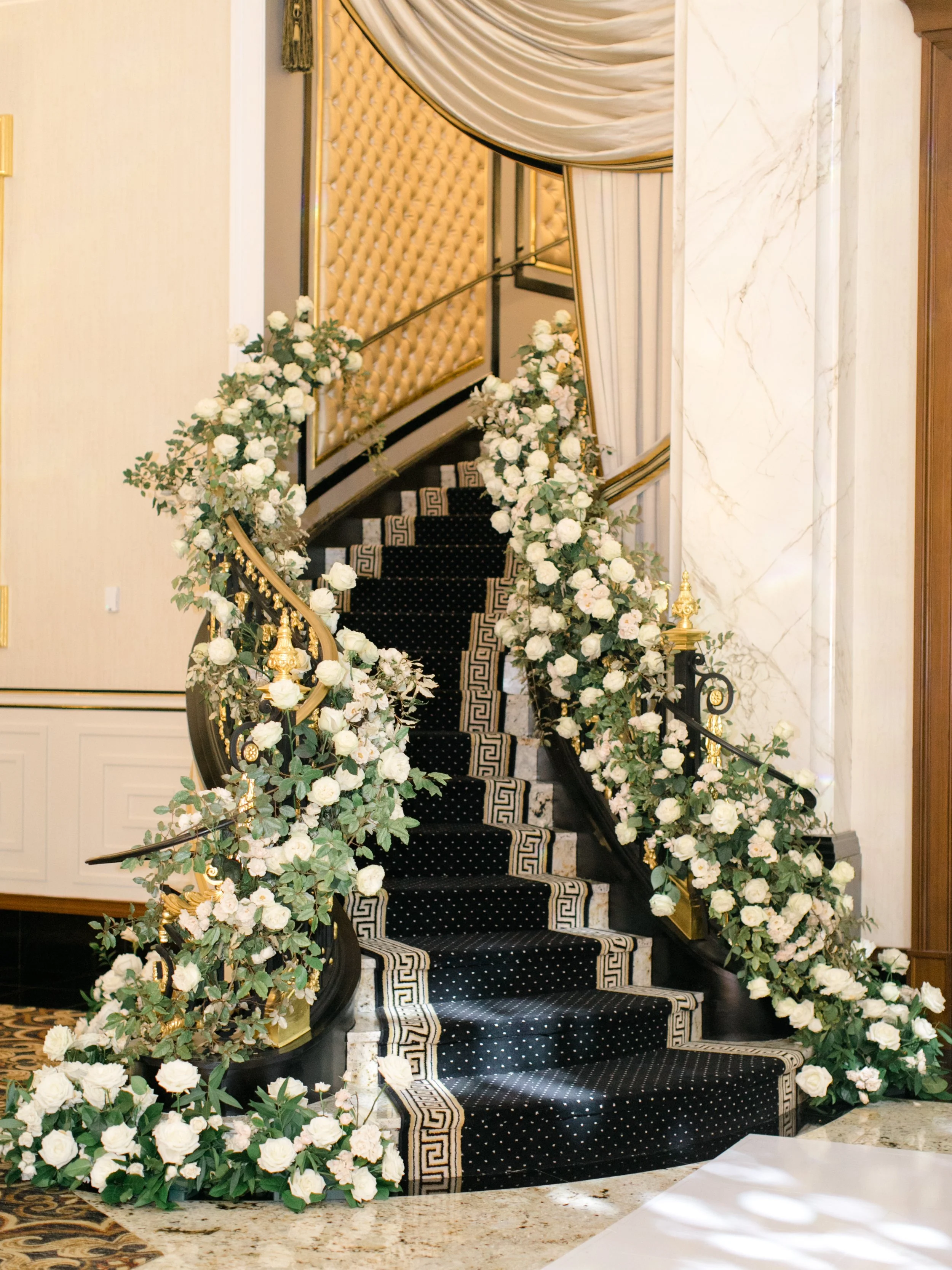 Decorated indoor staircase with black and white patterned carpet and white floral arrangements on both sides of the railing.