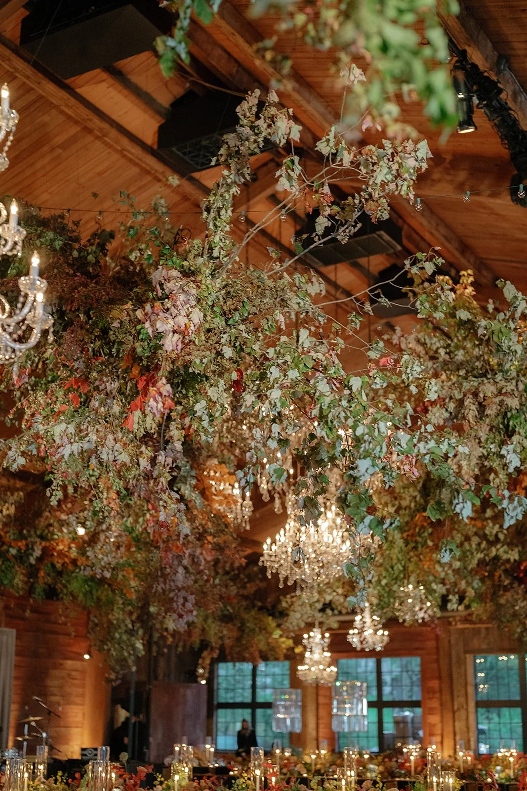 Indoor event space decorated with hanging greenery, large chandeliers, and table centerpieces.
