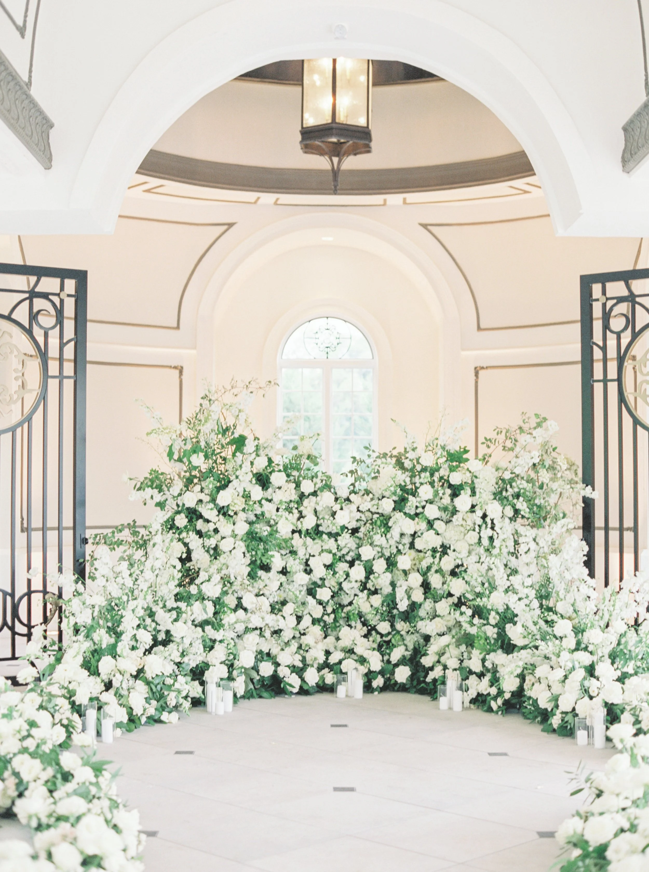 White floral arrangement in a venue with arched windows and elegant lighting for a wedding or special event.