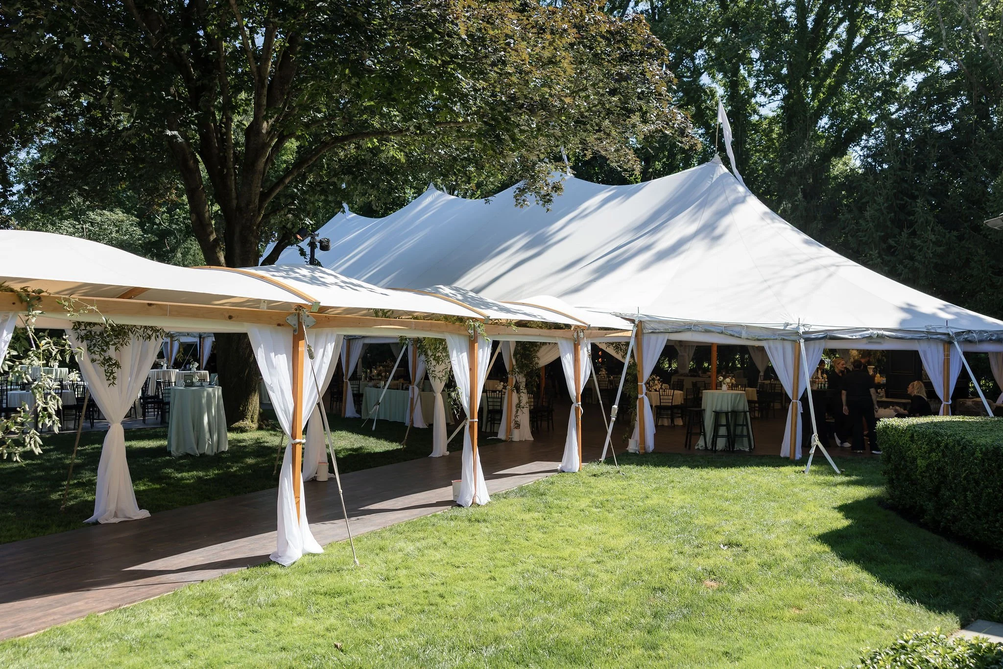 White event tents set up outdoors on a grassy area with trees, used for a celebration or gathering.