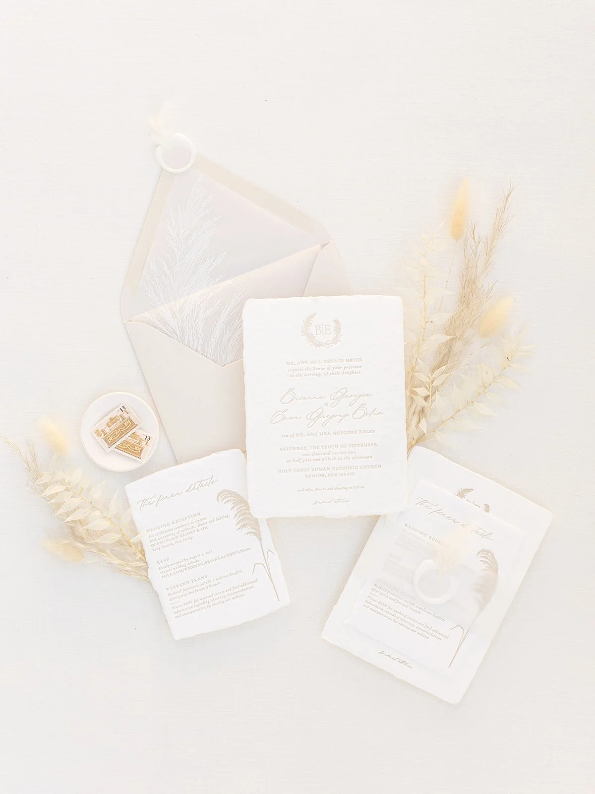 Wedding invitation suite with ivory and gold accents, includes RSVP card, wedding details, seals, and dried pampas grass on a white background.