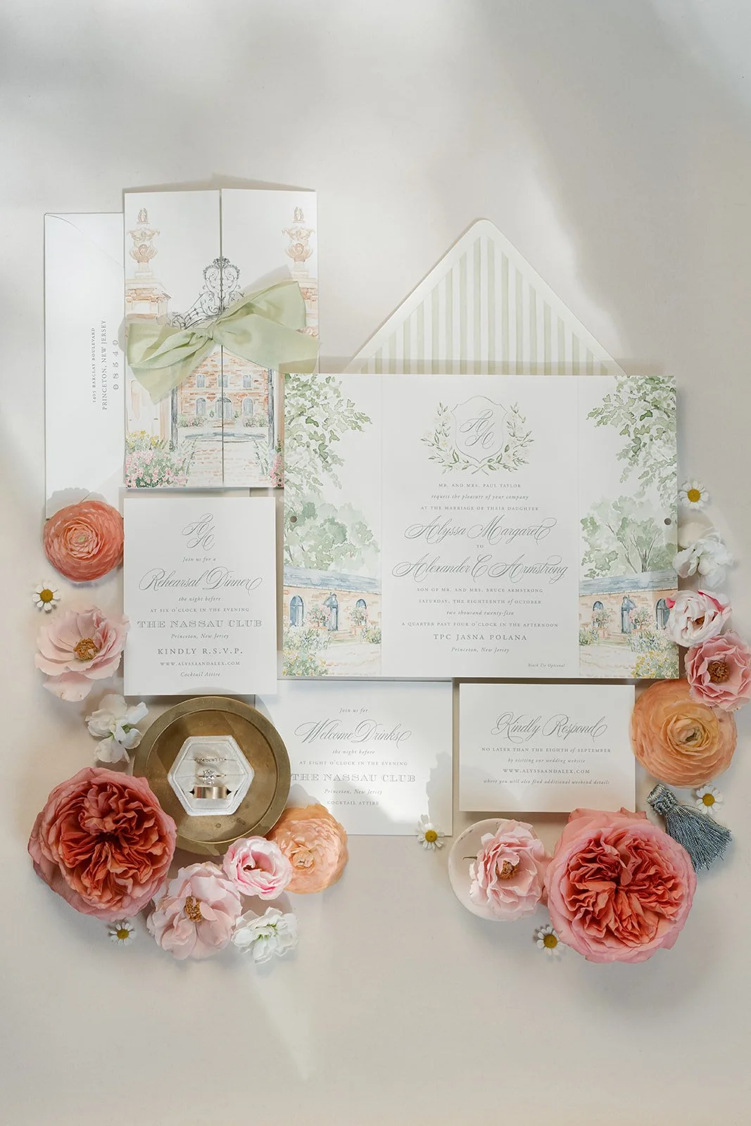 Wedding invitation suite with floral accents, rings, and a jewelry dish, arranged on a white surface with flowers and an envelope.