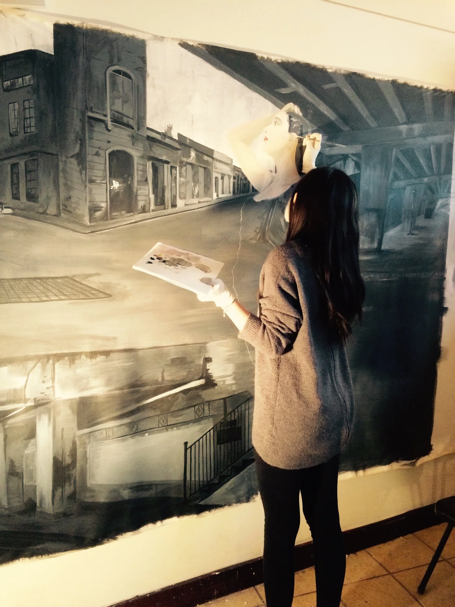 Student painting image of female over scene with buildings and overpass
