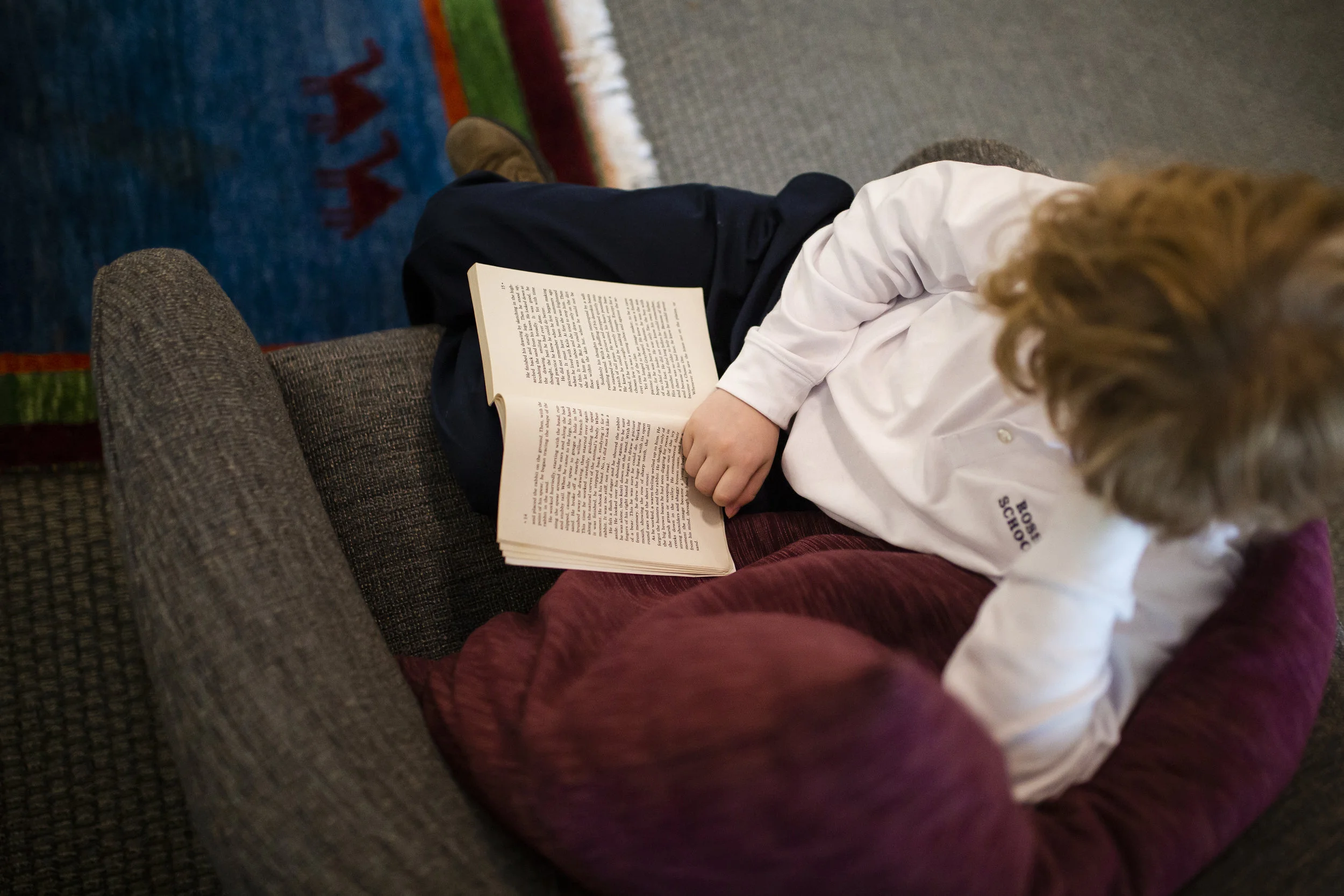 Ross Elementary student reading a book in a comfortable chair in one of the Ross School libraries.