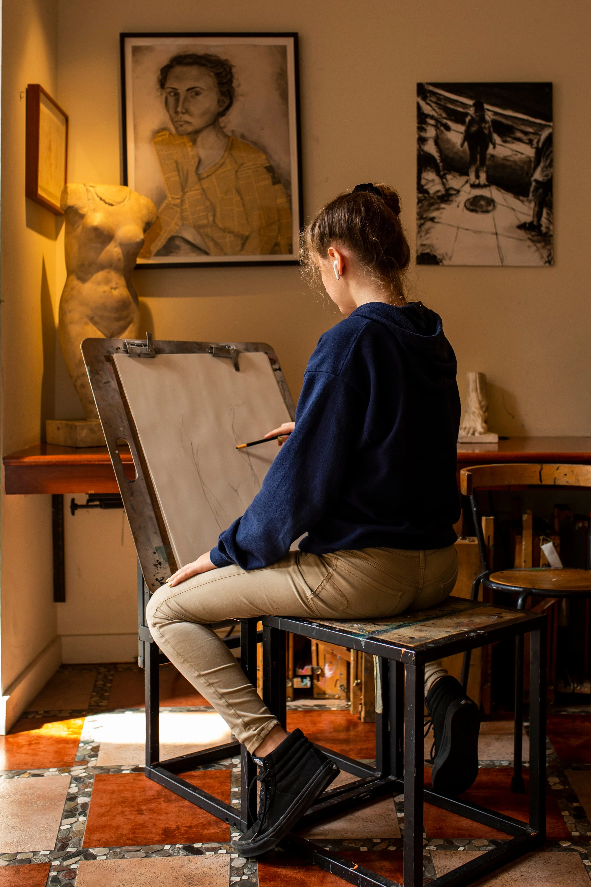 Ross Upper School student sketching at her easel, surrounded by replicas of iconic drawings and sculpture.