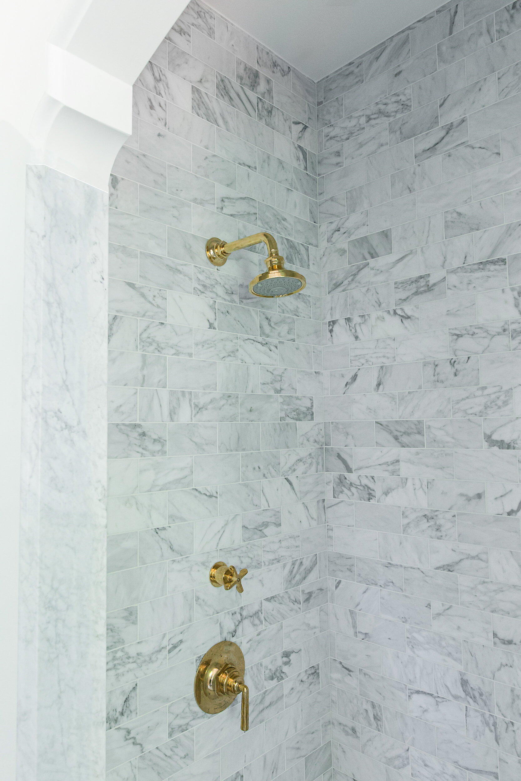 Bianco Carrara marble tiles in shower with gold faucets