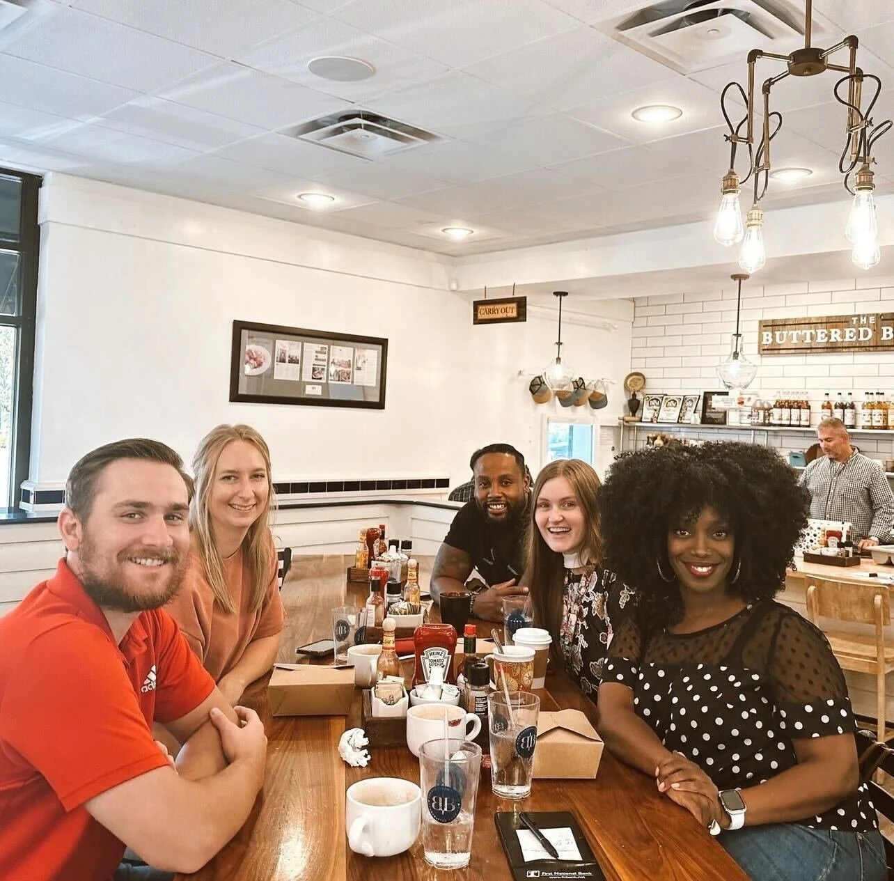 A group of five diverse friends sitting at a wooden table in a cozy cafe, smiling and enjoying each other's company.
