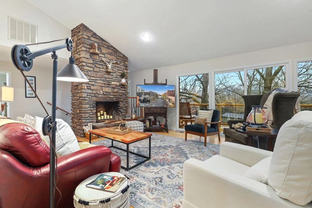 Welcome to the Woodland. When you walk through the front door, you'll immediately enter into our main living room, which is perfectly lit by our huge, floor-to-ceiling windows. Here, you'll see tons of seating including a red leather couch, three lou