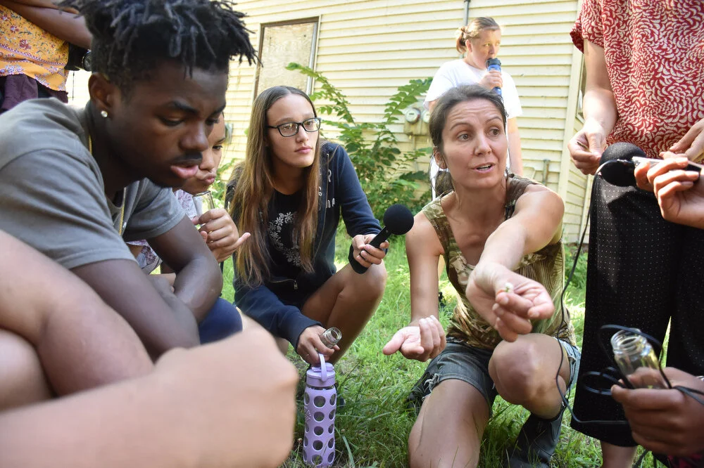  Ellie Irons, Uptown Summer mentor and Arts PhD student at Rensselear Polytechnic Institute, demonstrates to Uptown Summer youth how to collect seeds in Troy, N.Y. on July 19, 2018. The youth employees created a time capsule with native weedy species