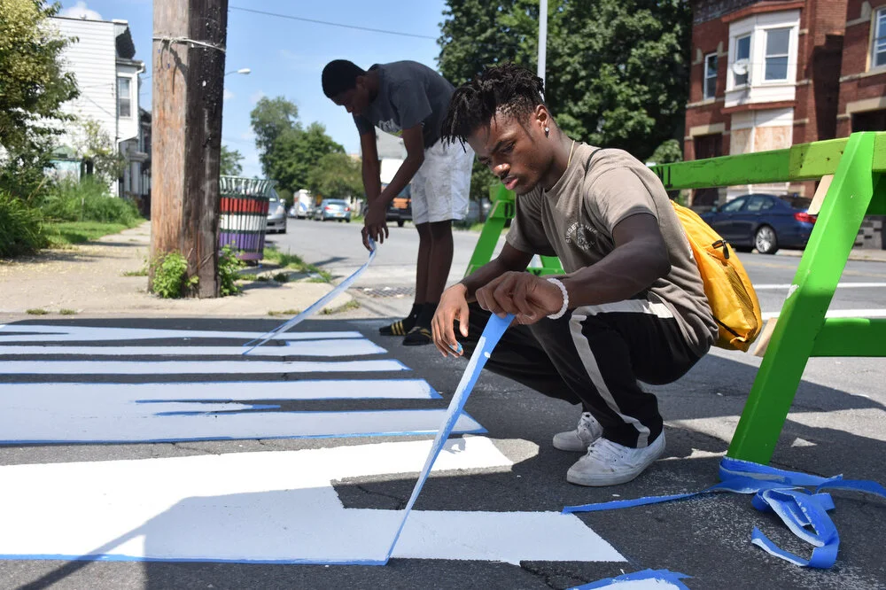  Donovan Wooten peels tape off of the youth employees “creative crosswalk” design down the street from the Sanctuary for Independent Media in Troy, N.Y. on Aug. 9, 2018. With the help of a local artist and poet, the youth painted words into new the c
