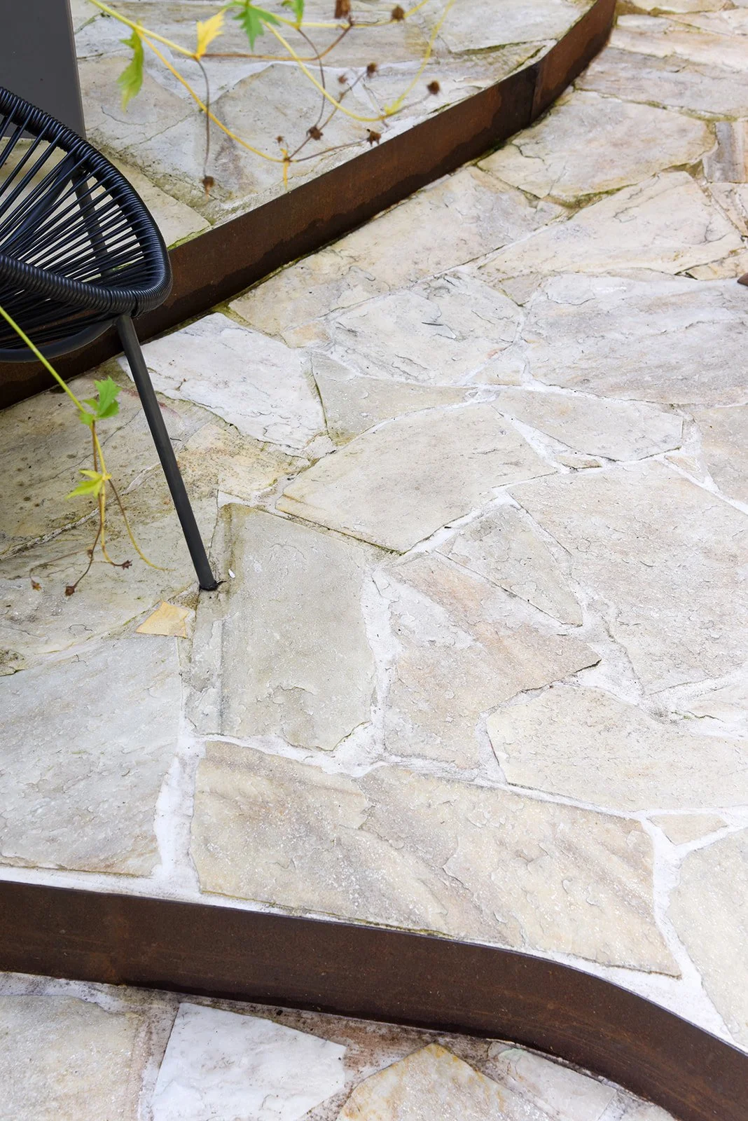Detail van een natuurstenen terras met cortenstalen afboording