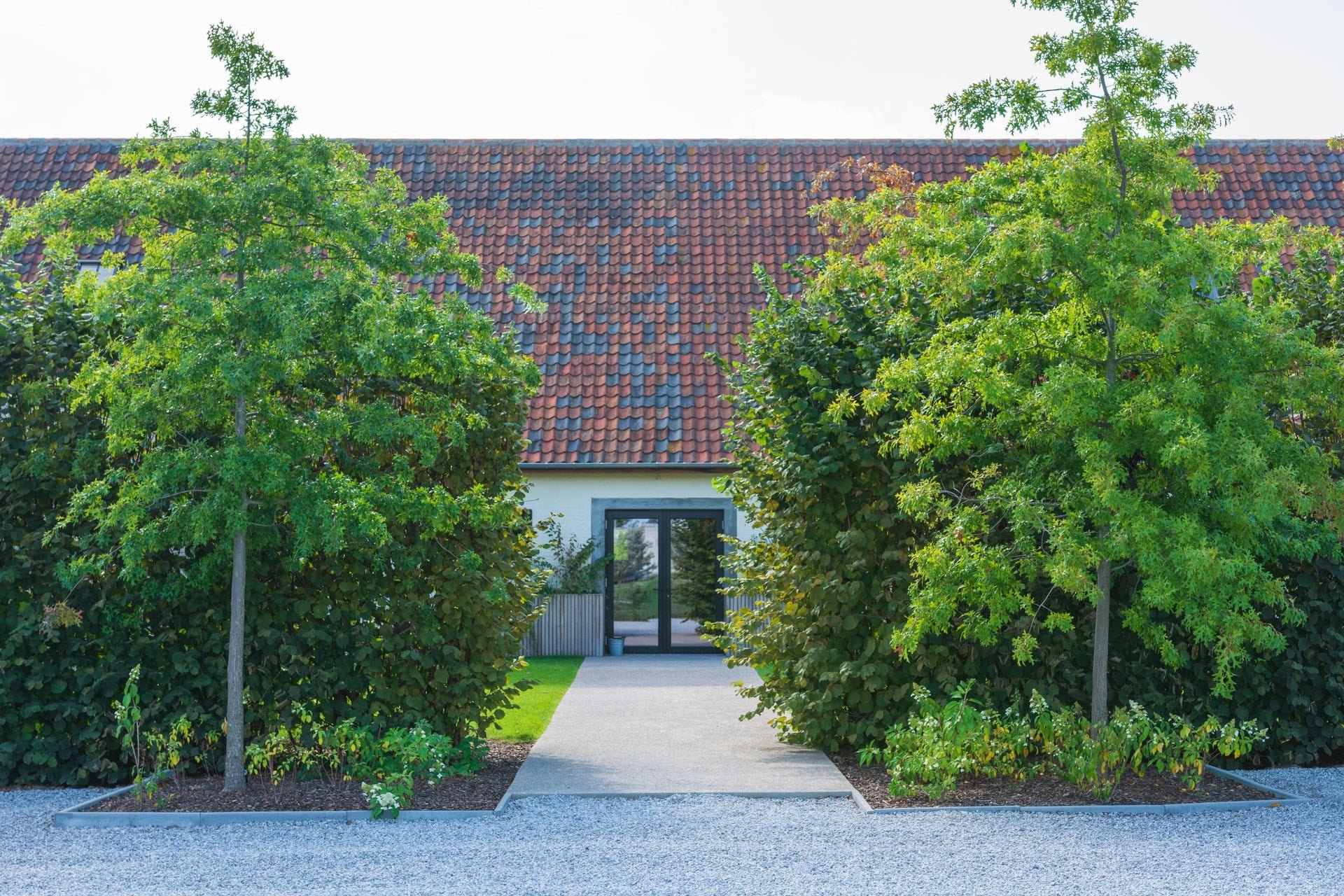 Grindpad tussen bomen en hagen naar de ingang van een bedrijfsgebouw
