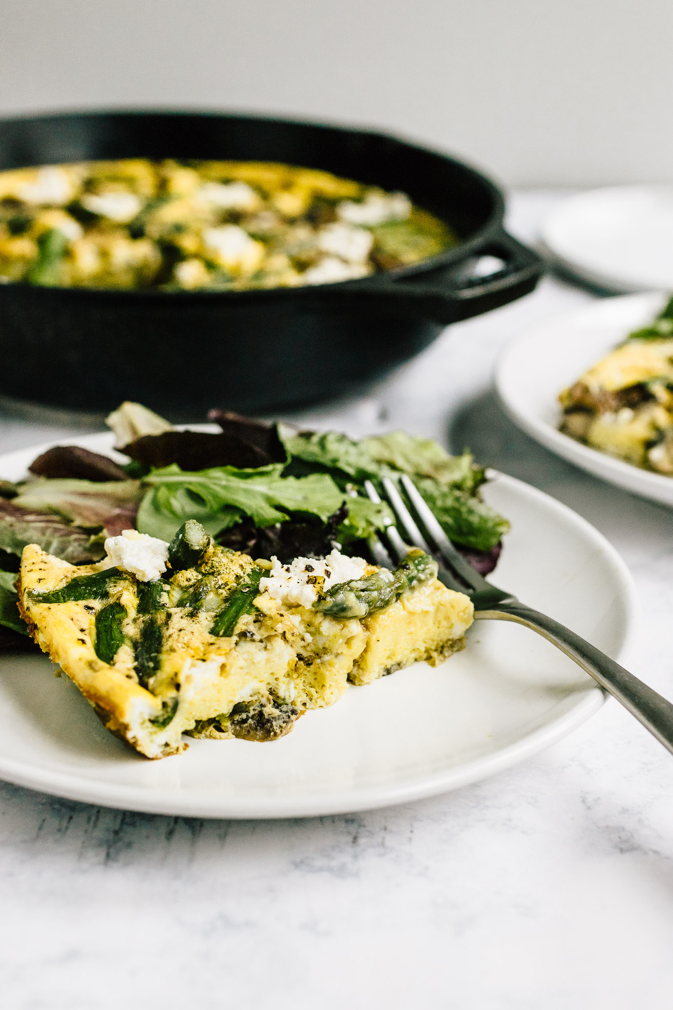 straight on view of slice of asparagus mushroom frittata with green side salad