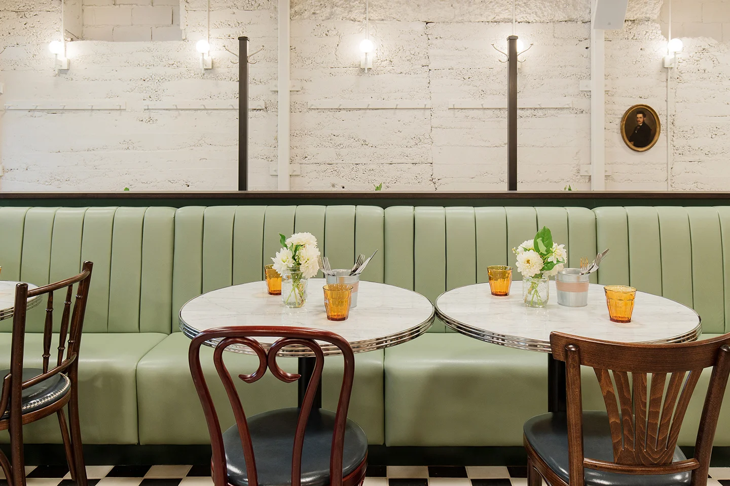 dining room - sea foam green booths with white marble round tables, wood chairs with leather seat. Behind booth seating is half glass partition and white cement wall.