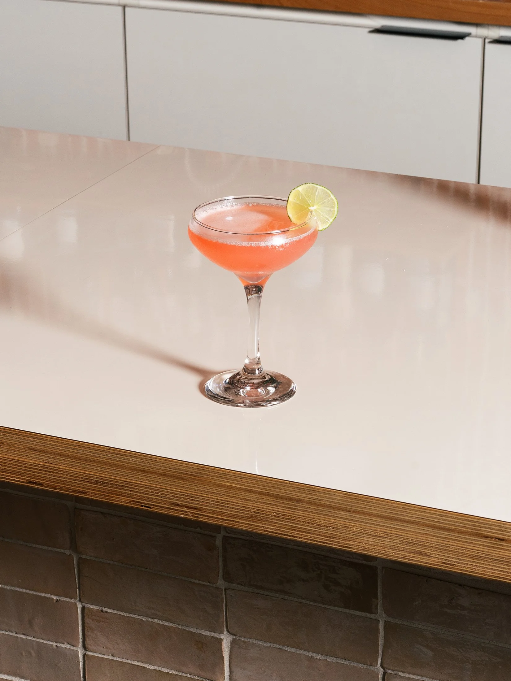 pink cocktail in a coupe glass with a lime twist
