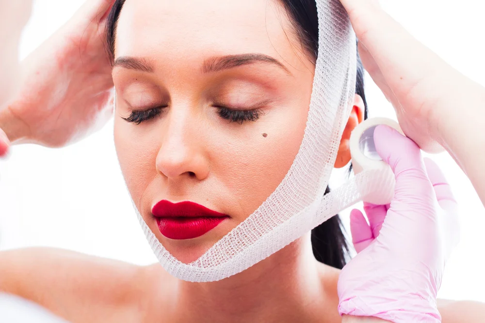 The doctor wraps the face of the patient with bandages after a facelift procedure.jpg