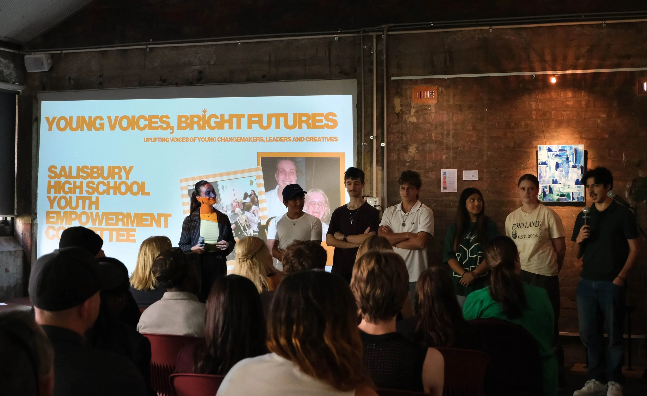 Salisbury High School Youth Empowerment Committee members are standing in a line at the front of the room, the person on the right speaks to audience