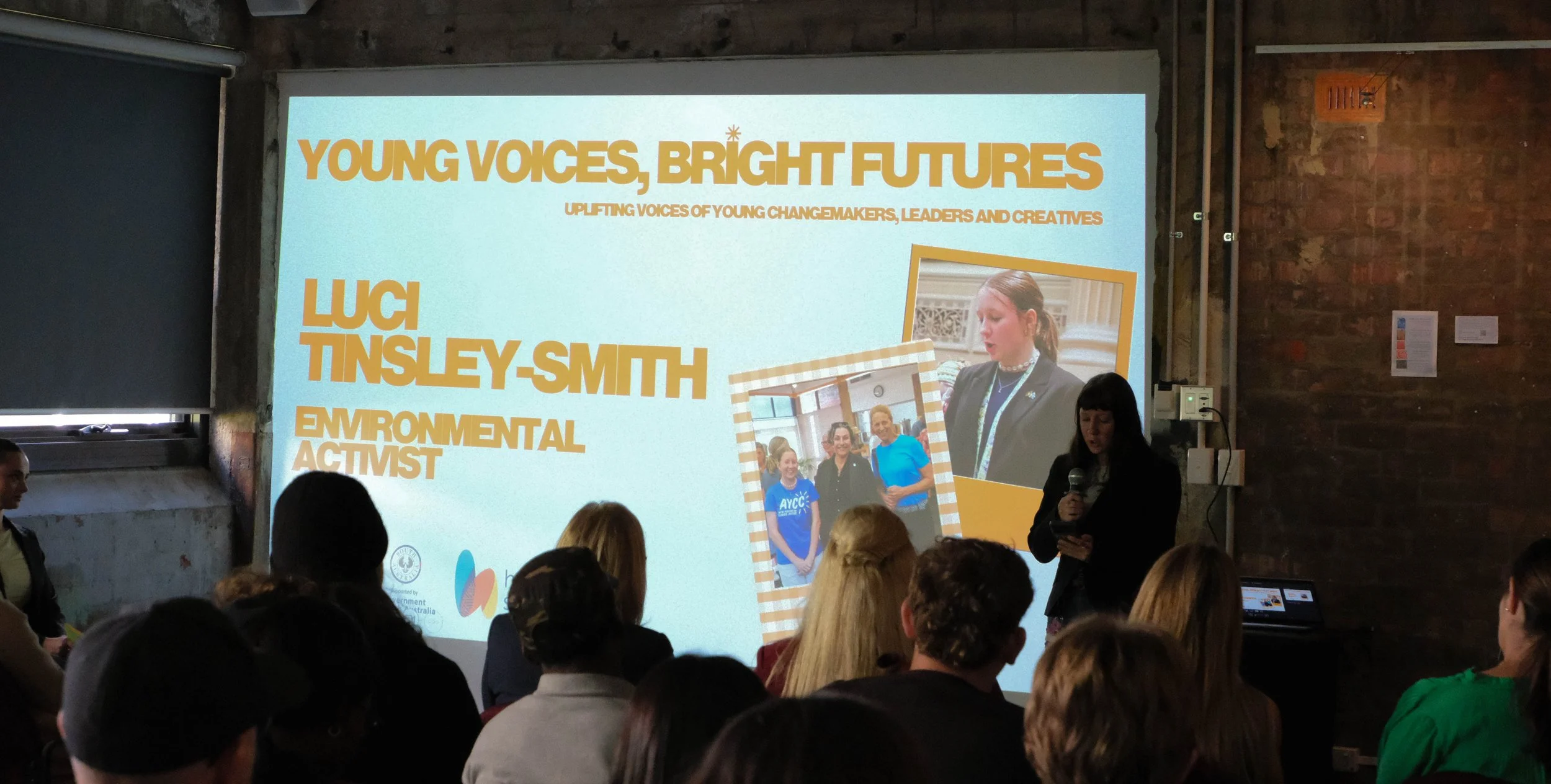 Luci speaks to audience in front of projector screen