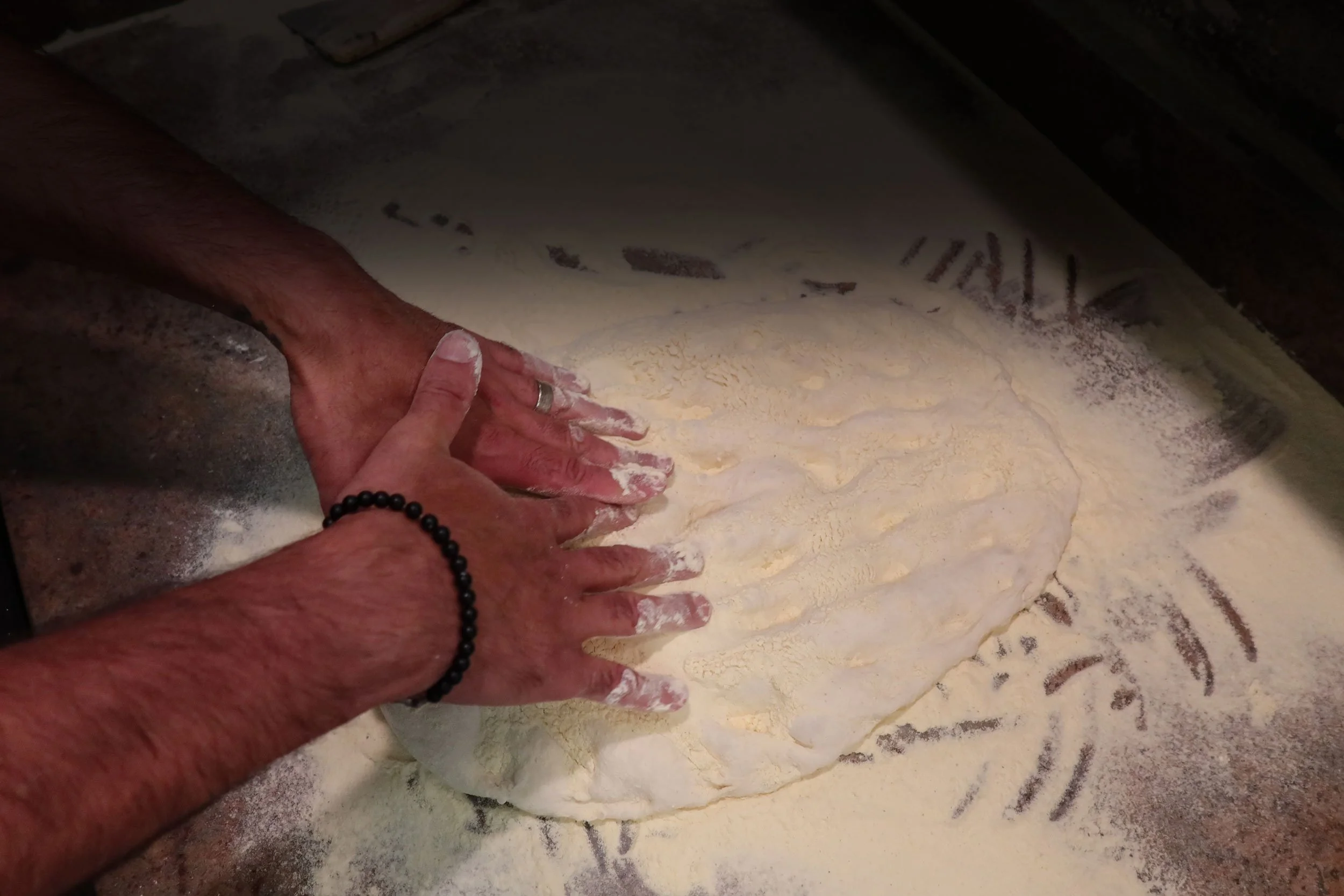 Close-up of hands kneading dough on a floured surface, with a dough scraper in the background.