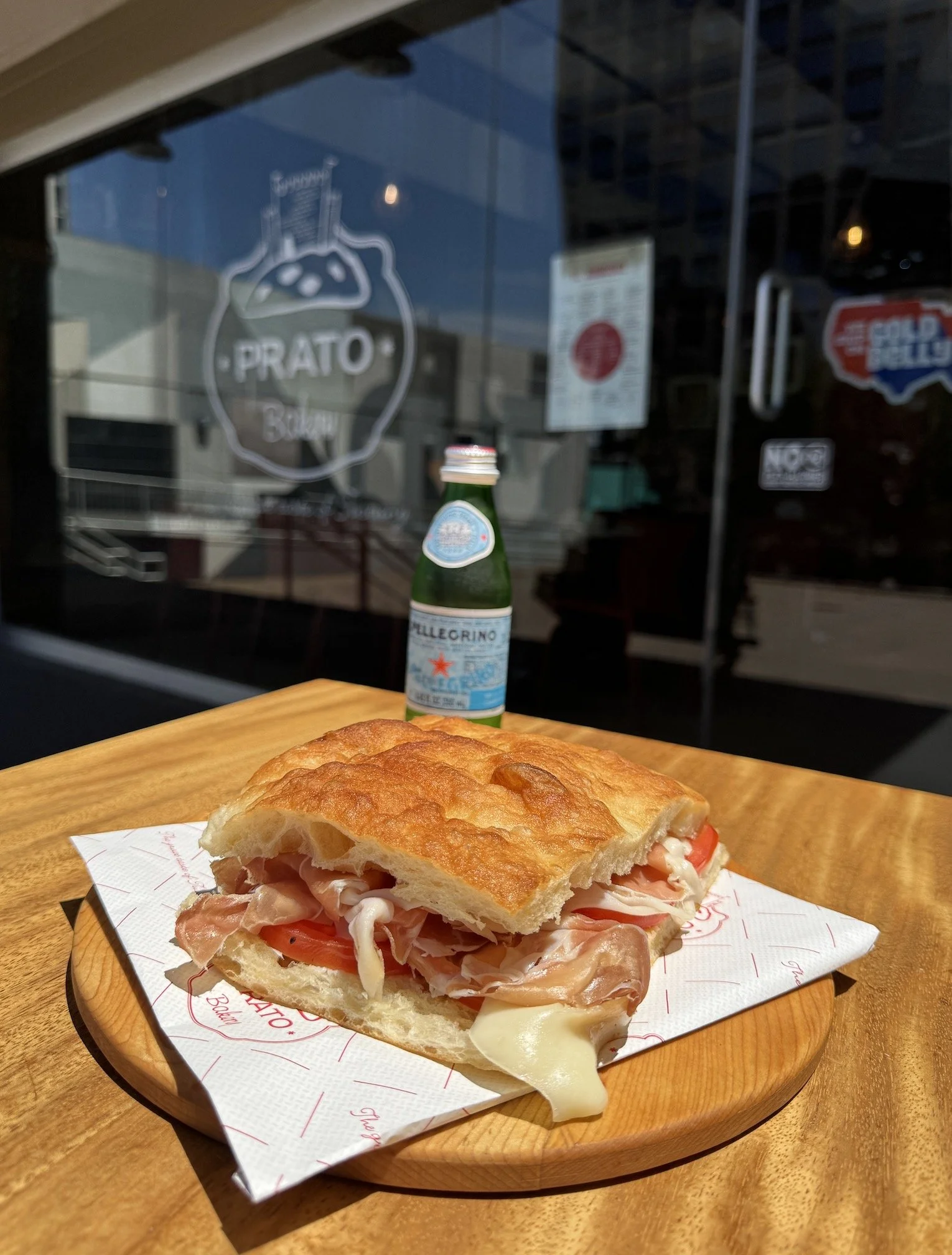 Sandwich with sliced ham, cheese, tomatoes, and lettuce on a wooden plate, placed on a table in a restaurant.