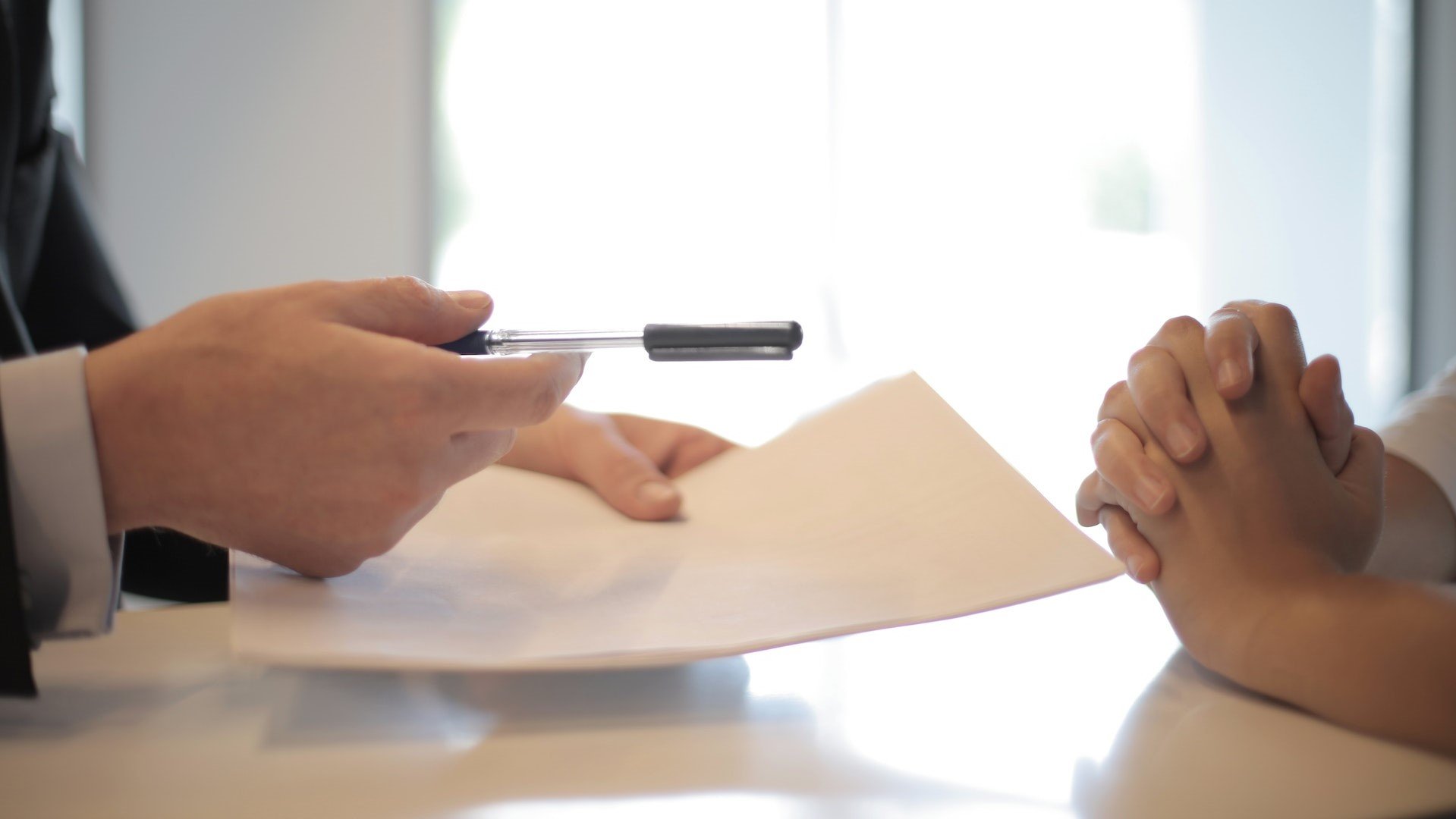 A lender hands a client a pen to sign some paperwork.