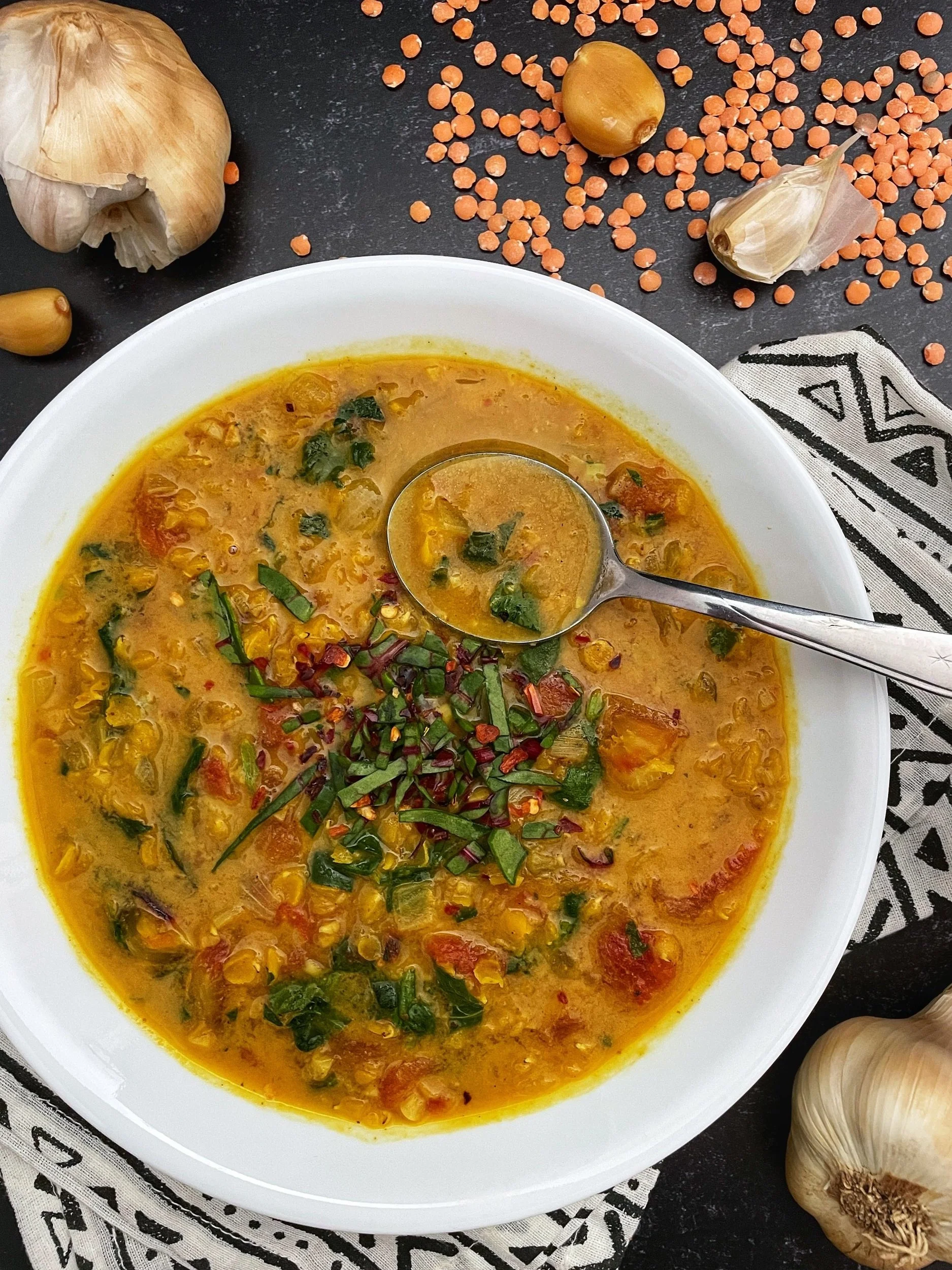 Smoked Garlic Lentil Soup is a lovely golden hue with flecks of greens and bits of red tomatoes.