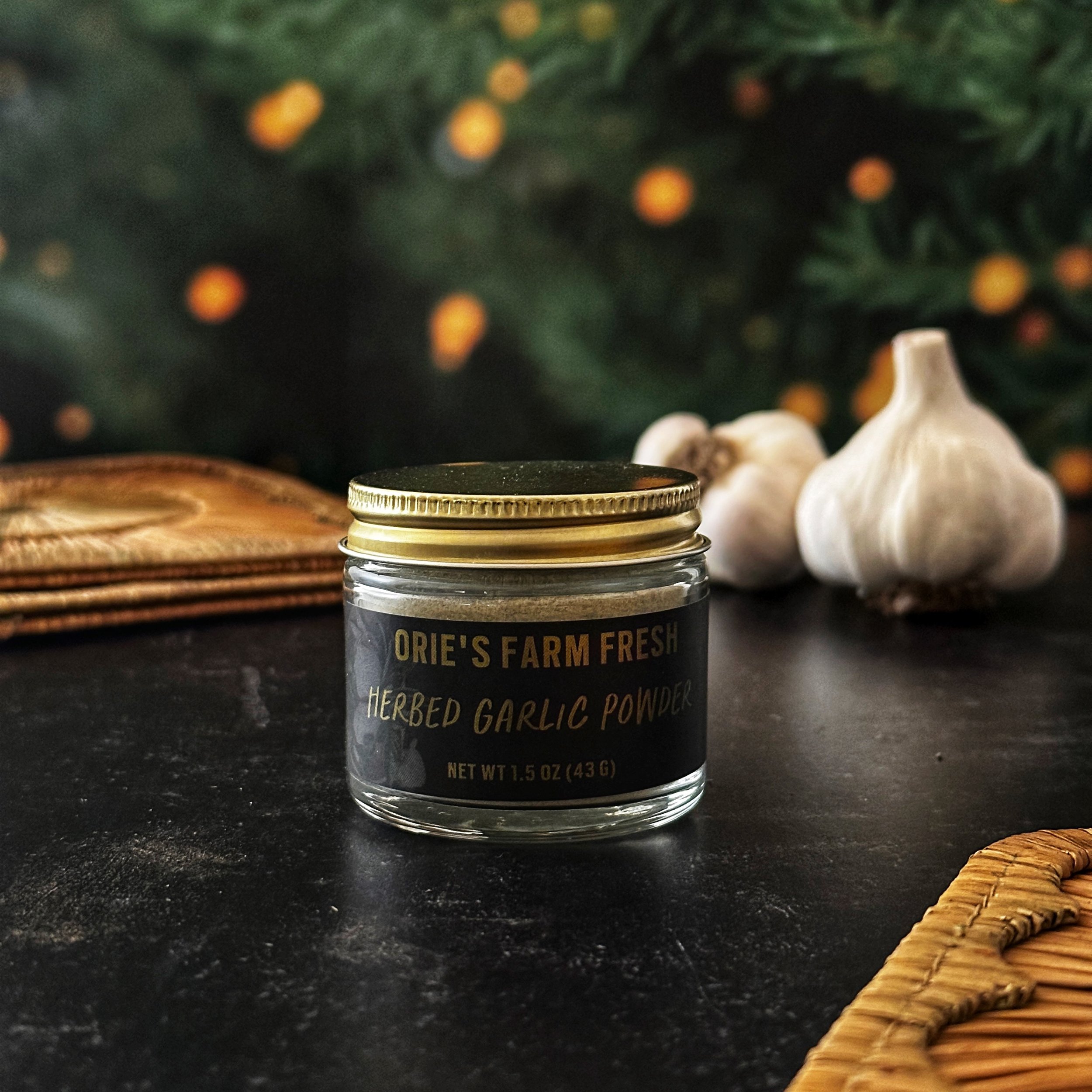 Jars of Herbed Garlic Powder with gold lids sit on a slate surface with a lit Christmas tree in the background.