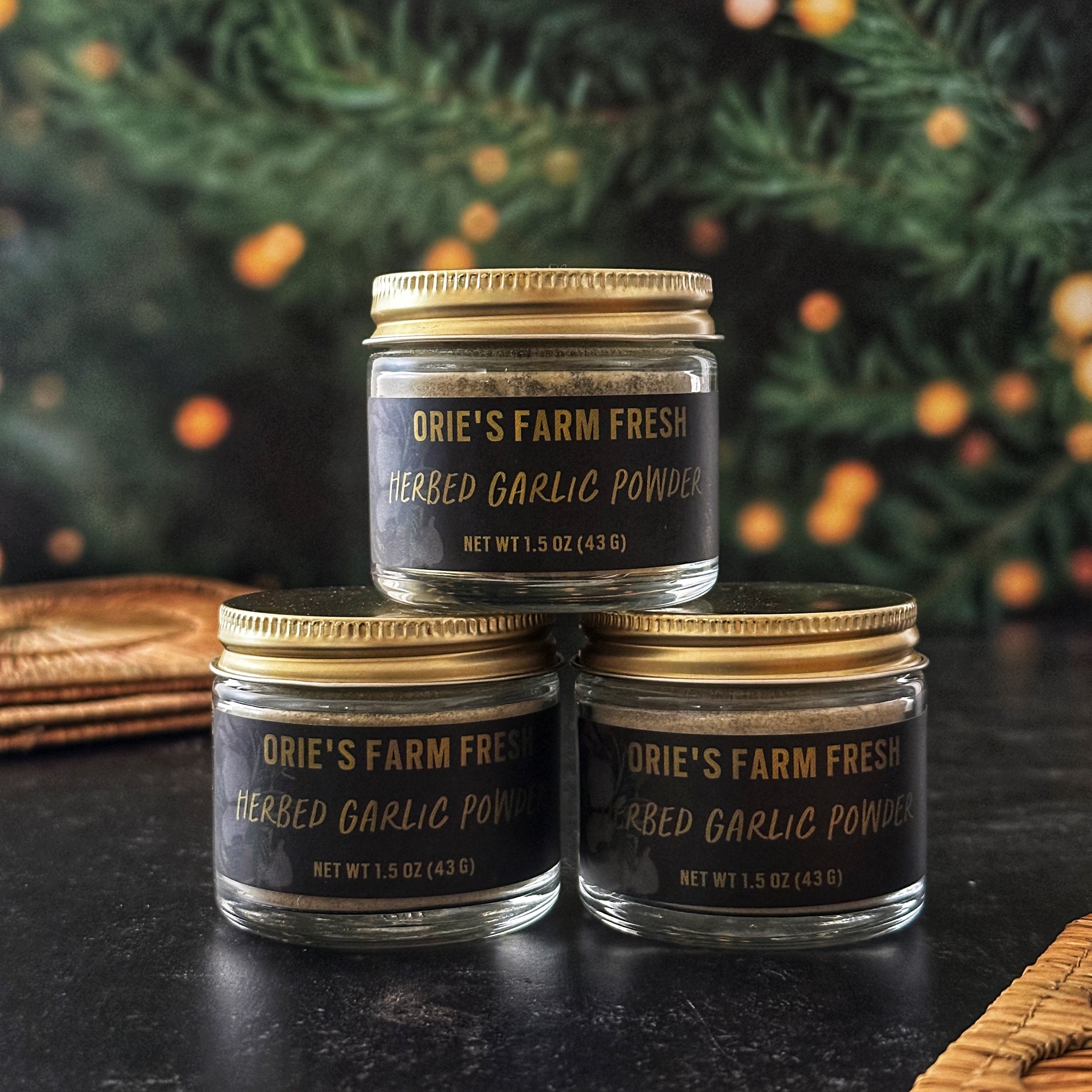 Three jars of Herbed Garlic Powder with gold lids look festive in front of a lit Christmas tree.