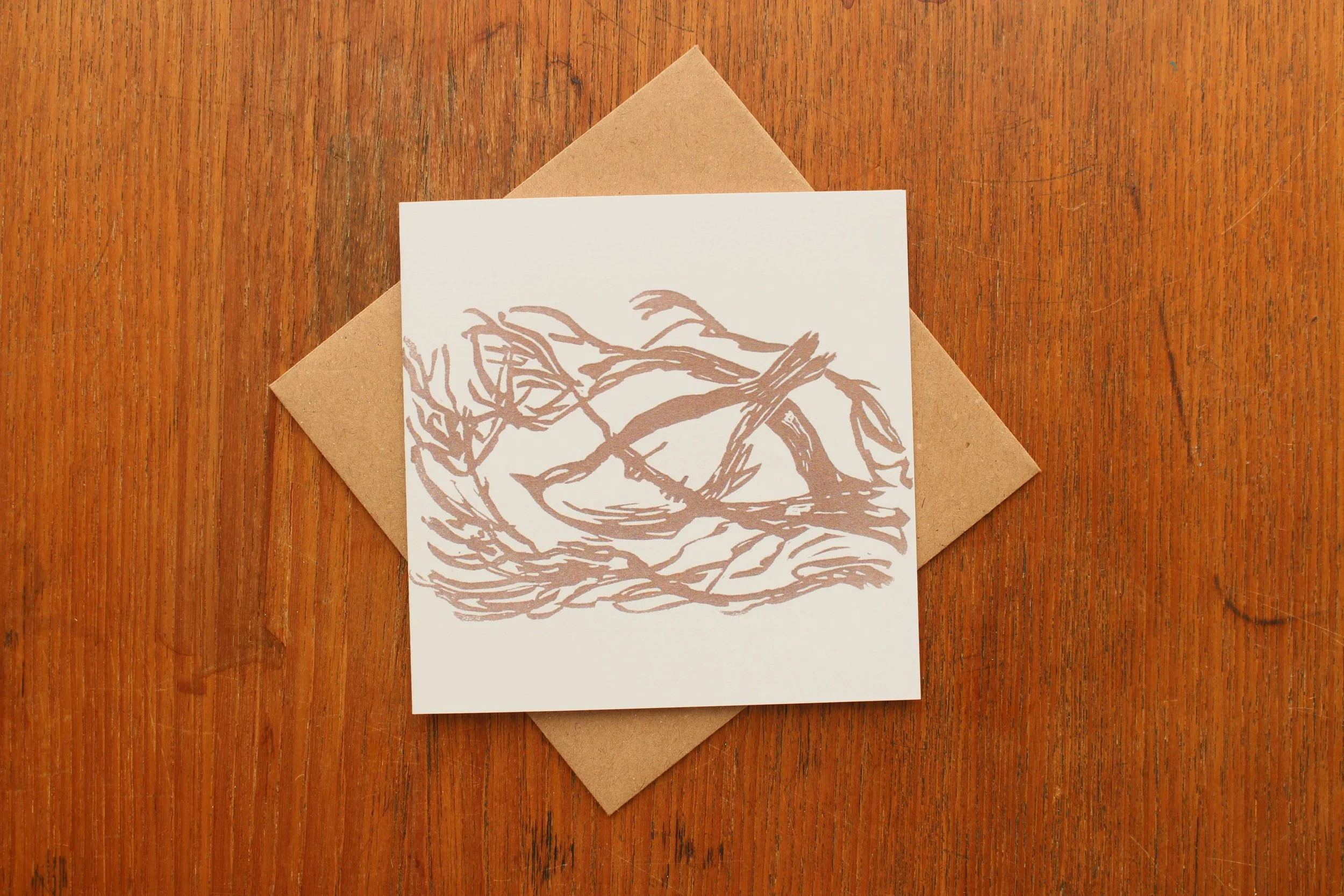 January Storm is a linocut print showing a sparrow sheltering from the weather in the bare branches of a tree. The photo shows a greeting card reproduction of the original linocut by Cat Moore