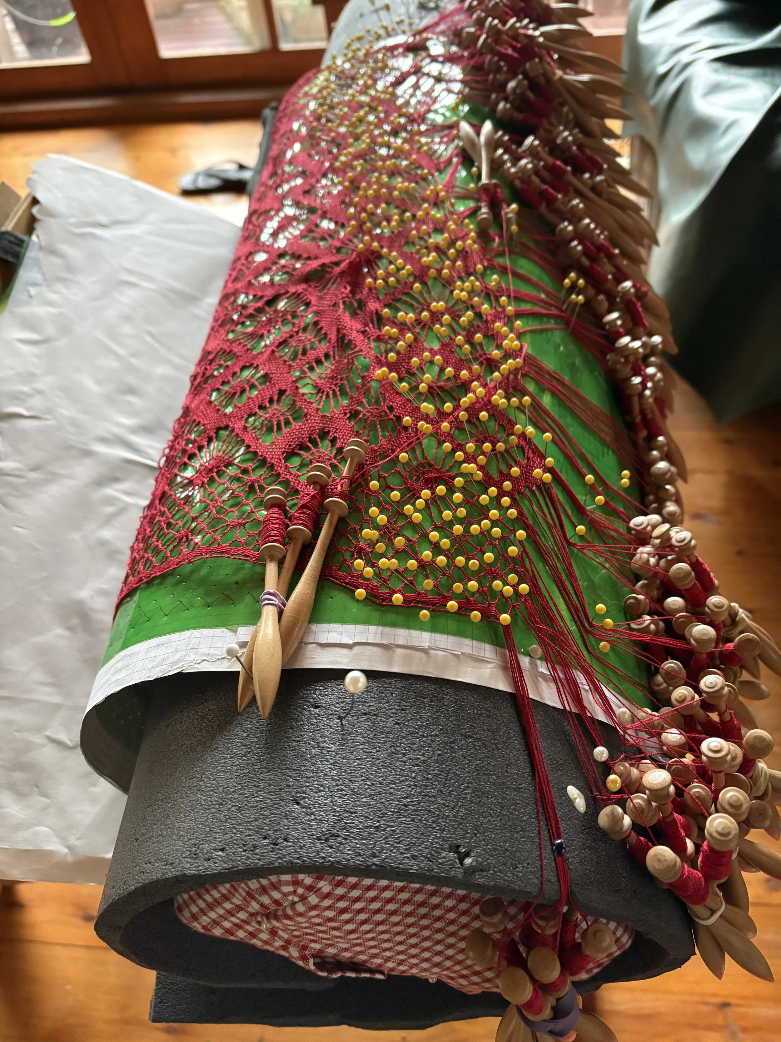 Looking along the pillow. The design is wrapped around the pillow, the work is rolled up as the lace is made  while the pins slowly follow down the pattern and thread is knotted.