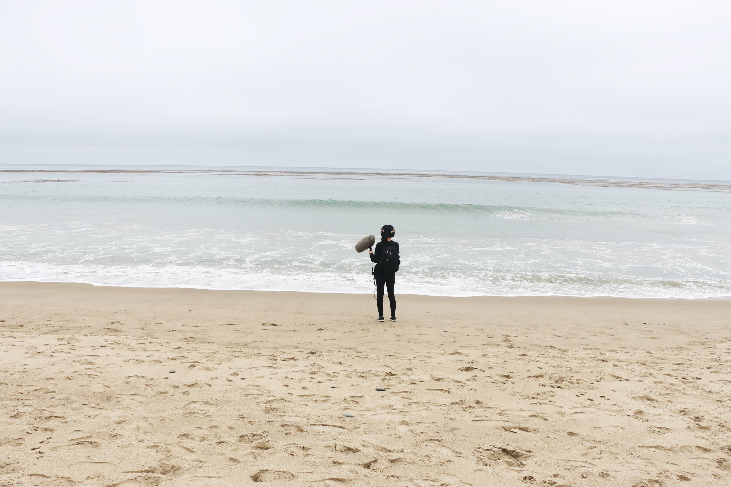 Host/producer Paola Mardo records sounds on a beach in Malibu, California. Photo by Patrick Epino.