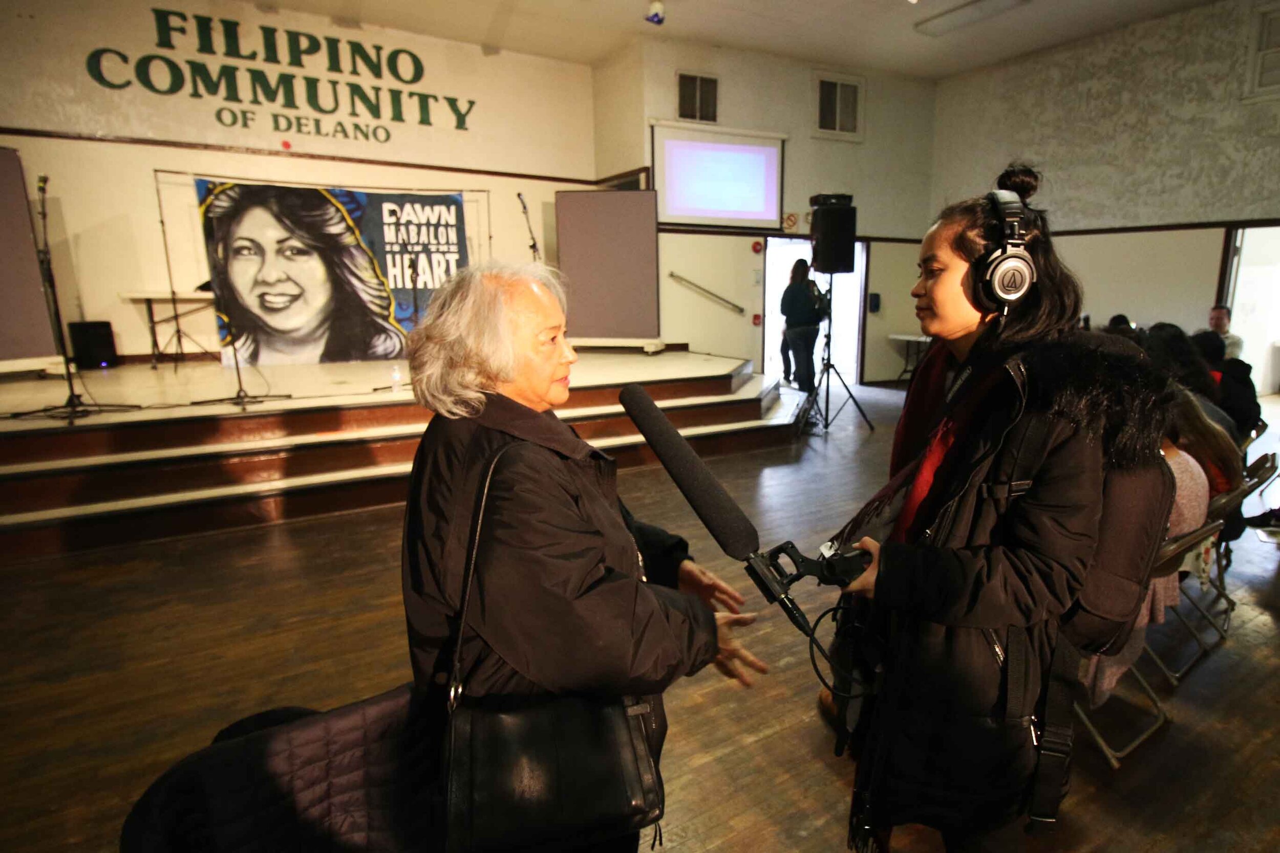  Long Distance Host/Producer Paola Mardo interviews Christine Bohulano-Block against the backdrop of a mural for her late daughter Dawn Bohulano Mabalon at Filipino Hall in Delano, California. 