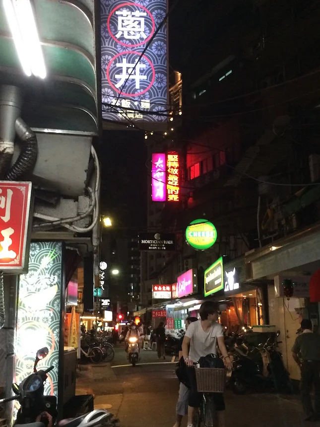 Typical back-street view at night in Taipei, with bicycles, motorbikes, lights, sounds, and smells