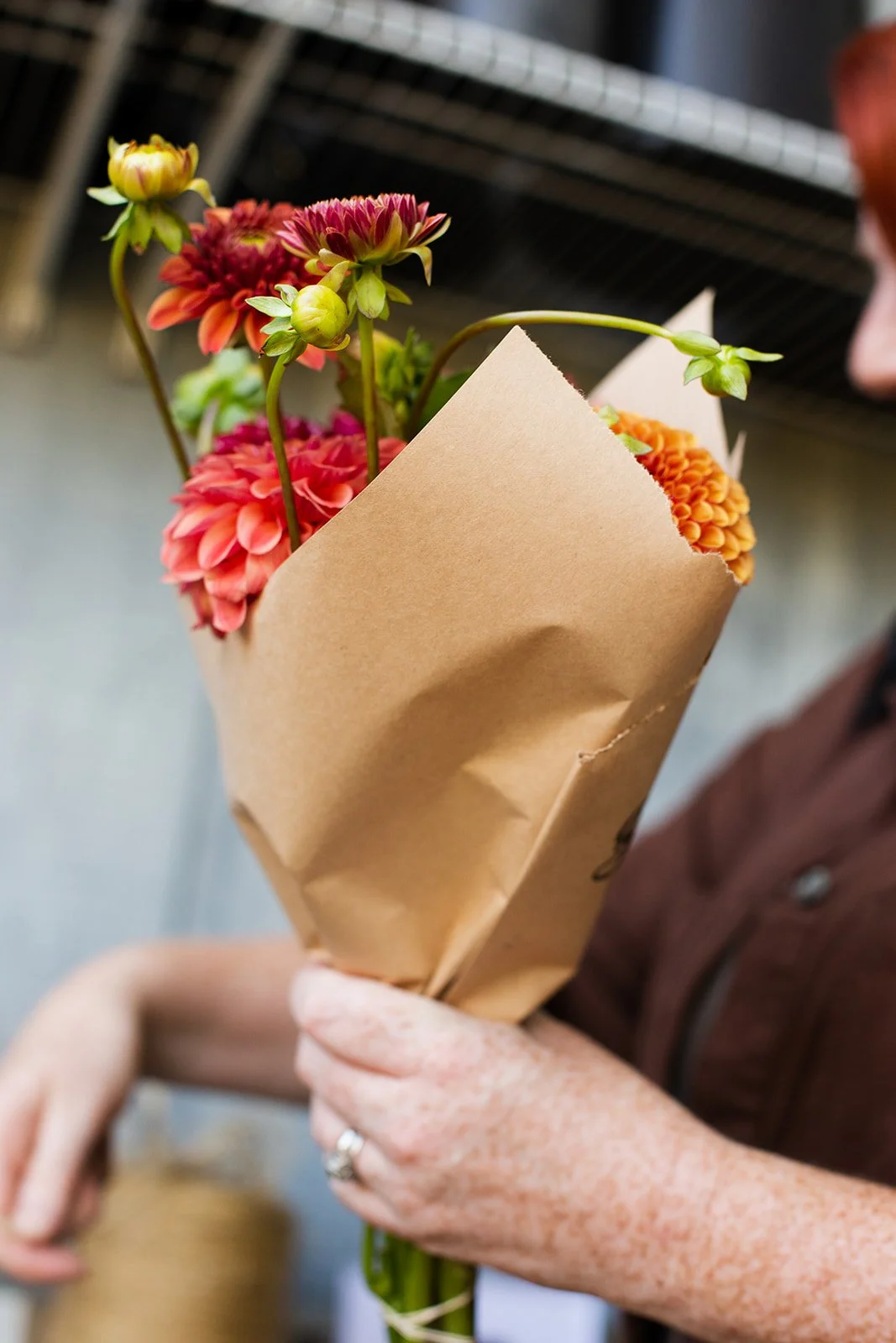 A person holding a bouquet of colorful flowers wrapped in brown paper.