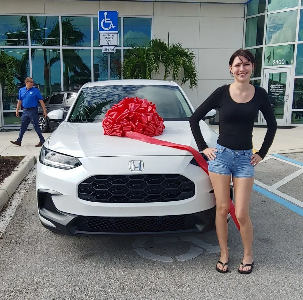 Young woman smiling and standing next to her brand new Honda with big bow on the hood