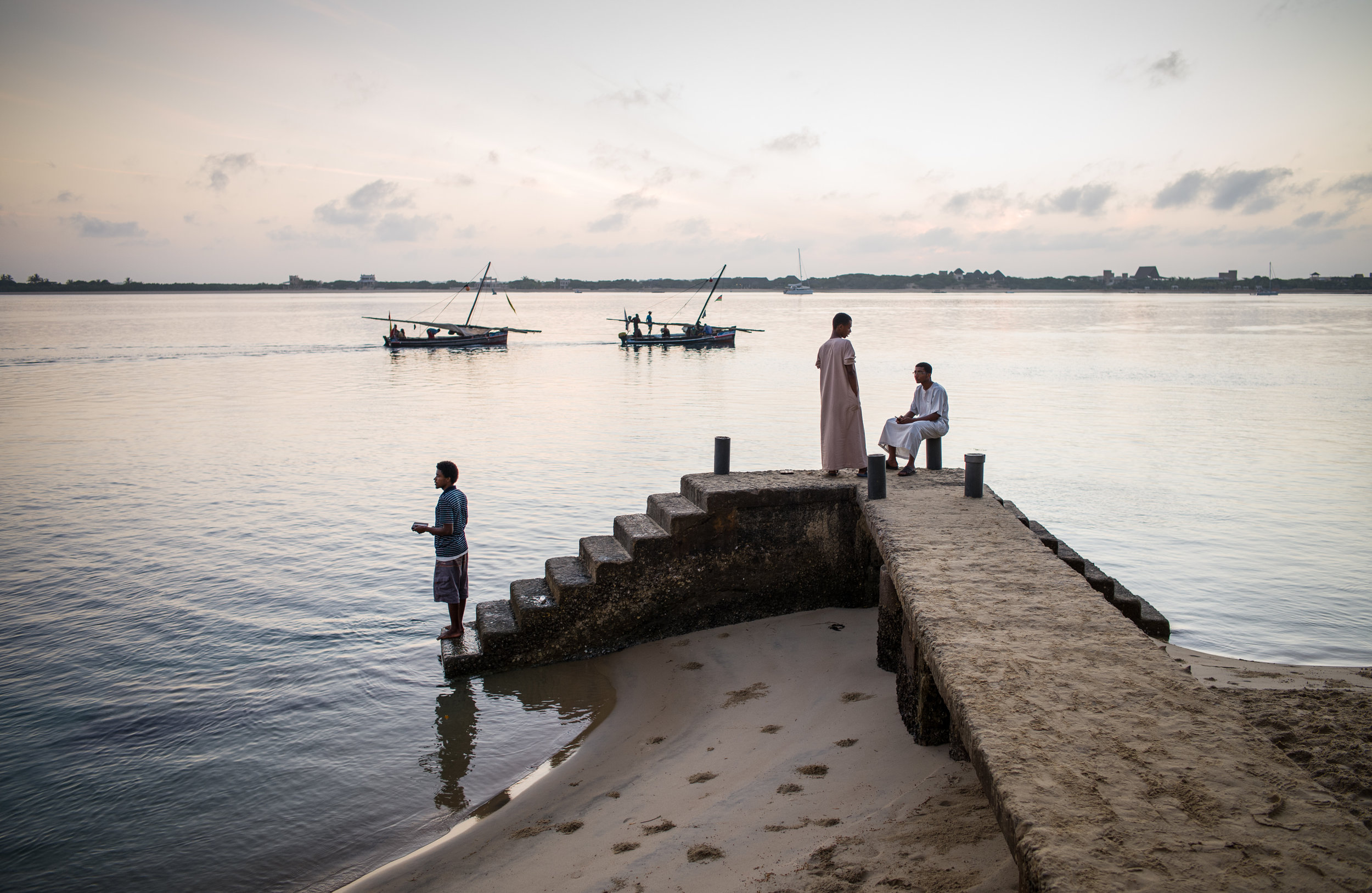 Young men linger on Shella pier on Lamu Island in Kenya as fishermen head out to sea aboard their jahazis – a type of dhow sailing vessel