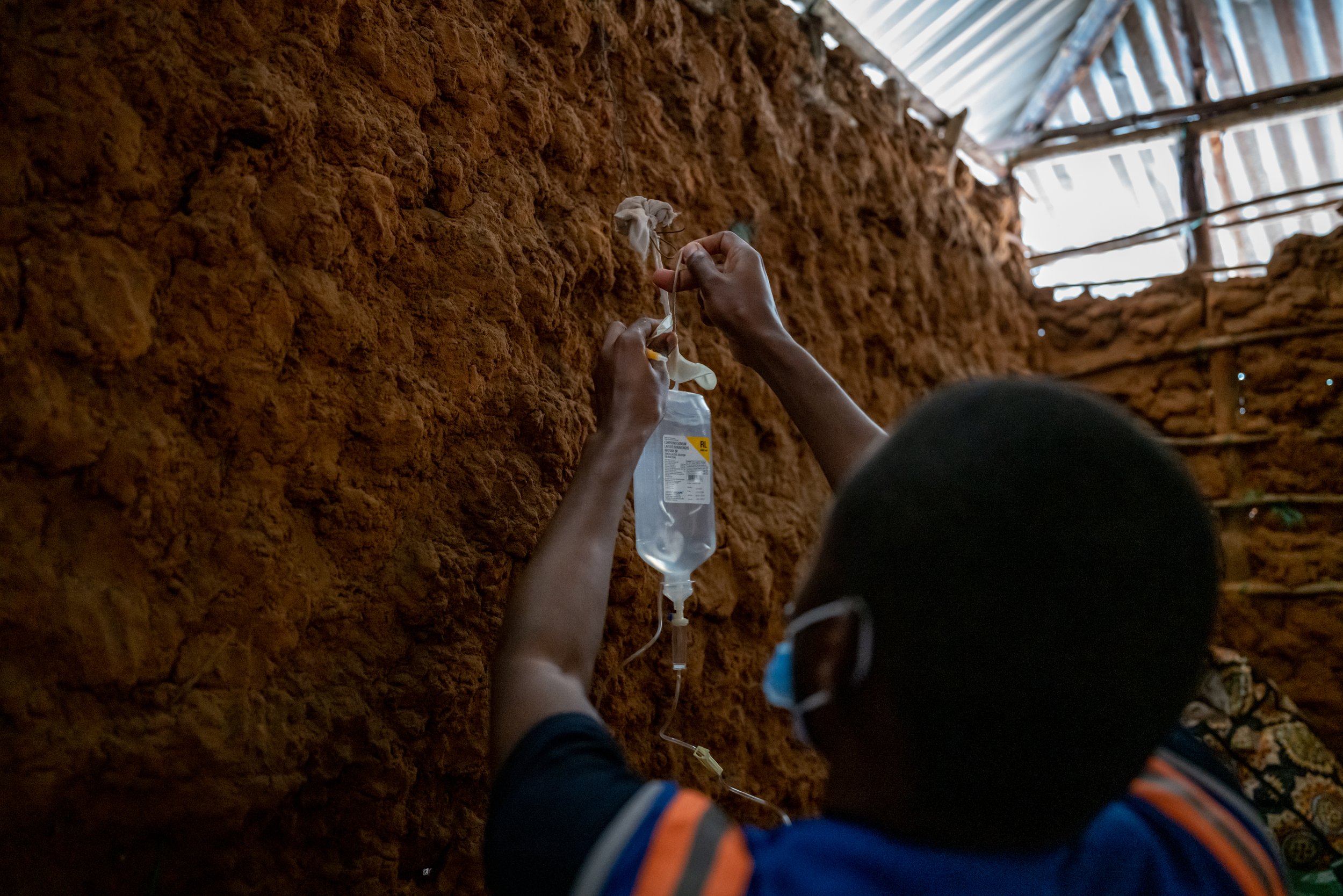 Jackson Mugambi hangs a bag of IV fluids for Omar Shongwa on the wall of Shongwa’s mud hut in the village of Bahamisi, Kenya